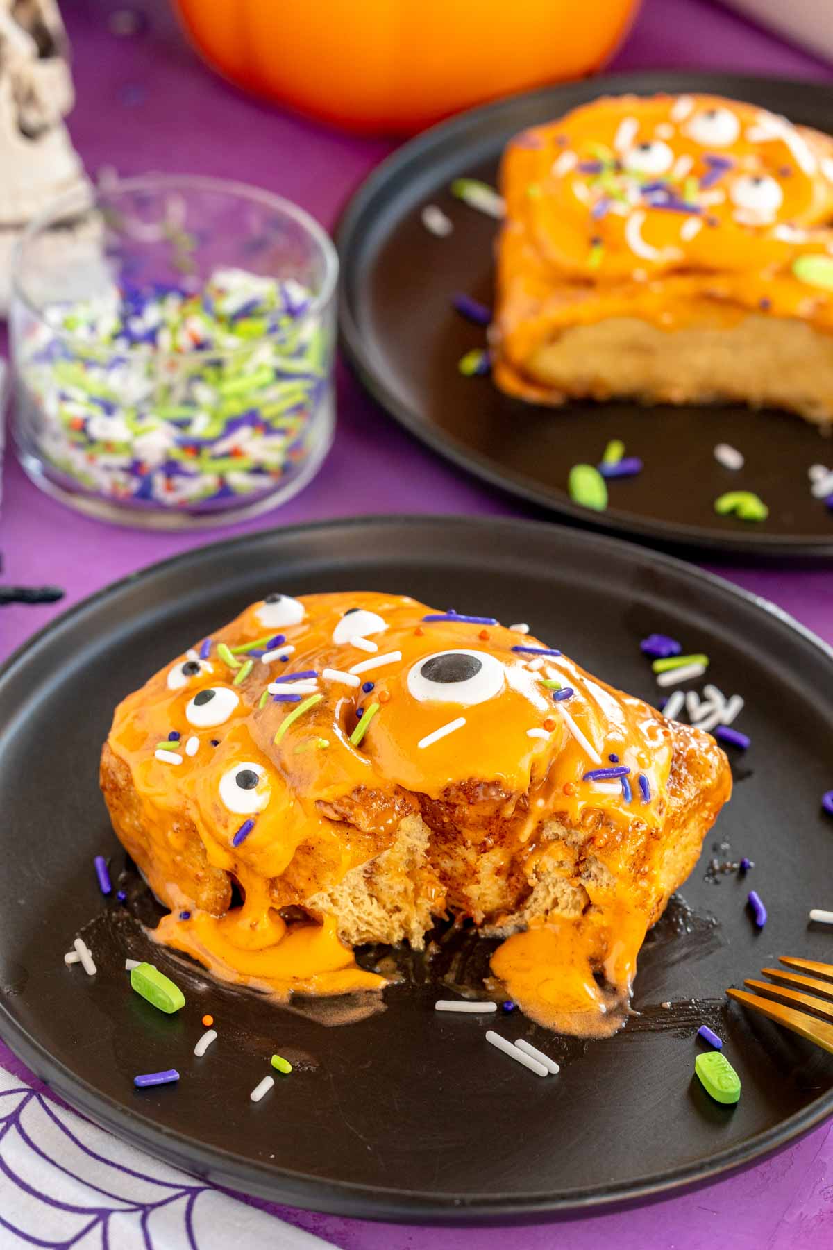 Halloween cinnamon roll on a black plate with a bite taken out of it