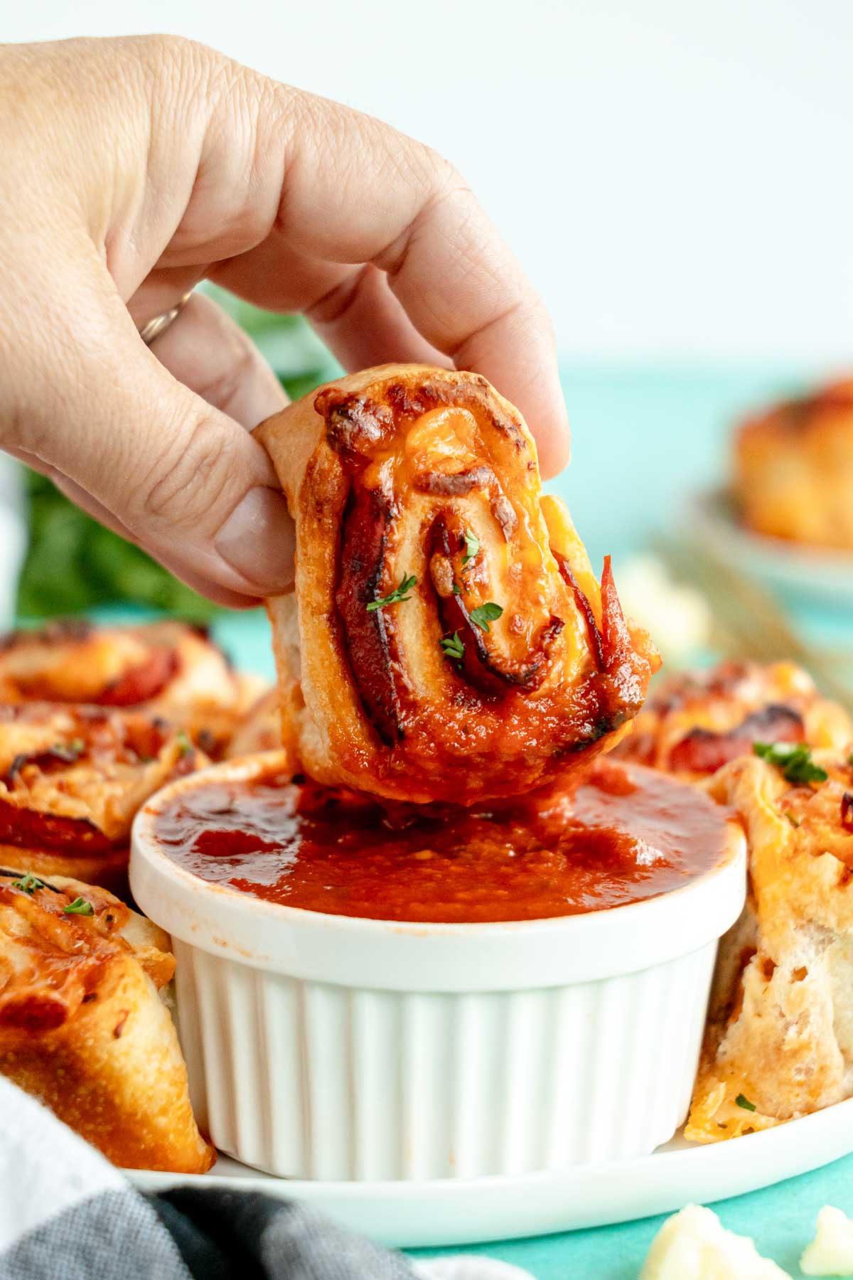 hand dipping a pepperoni roll in a white ramekin with pizza sauce