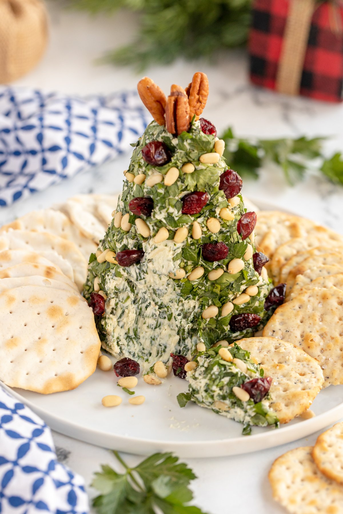 Christmas tree cheese ball surrounded by crackers with part of the cheese ball scooped out