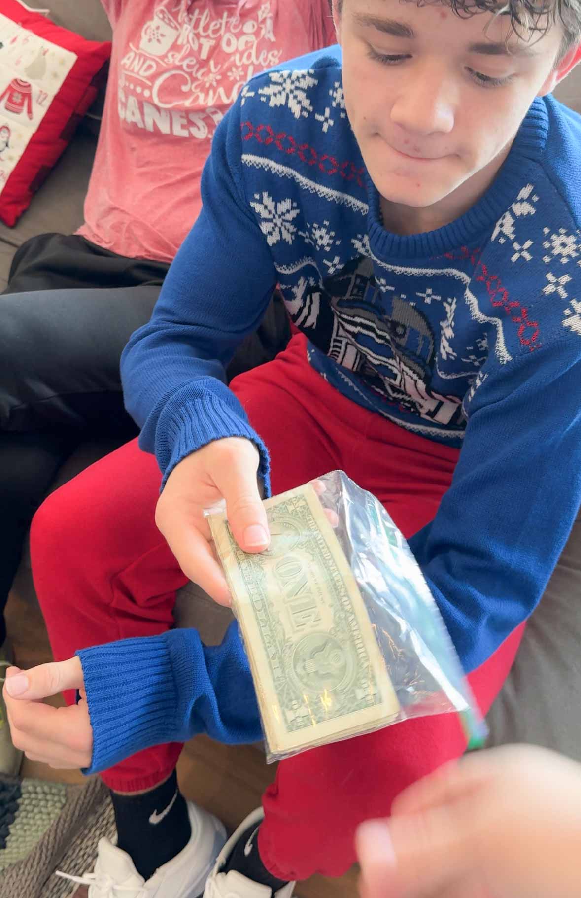 a teen boy holding a bag with $1 bills inside