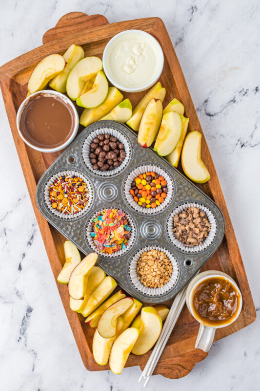 caramel apple bar toppings on a wood board