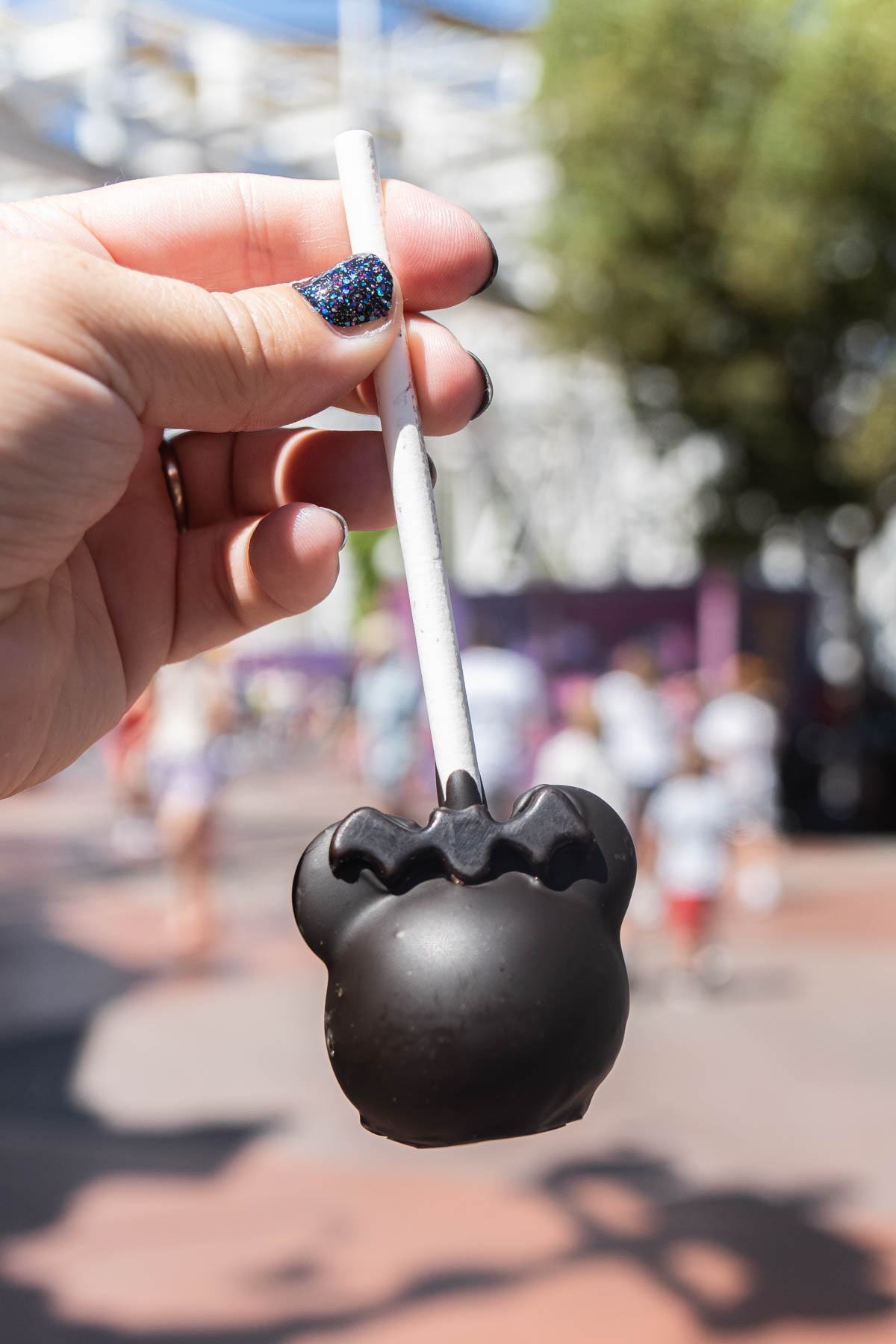 Hand holding a Minnie cake pop at The best Disneyland Halloween food! Disneyland treats, drinks, and more to try during Disneyland Halloween time!