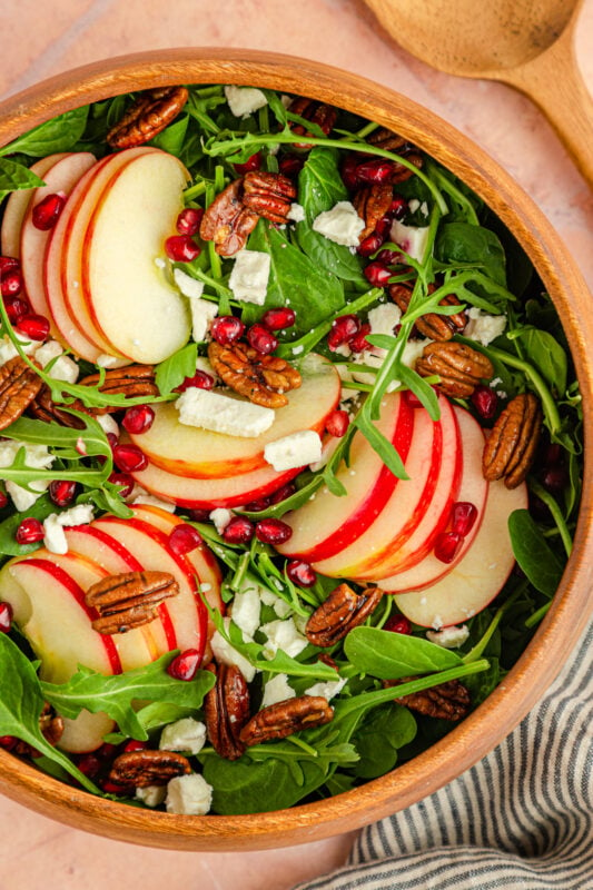 pomegranate feta salad with apple slices in a wood bowl