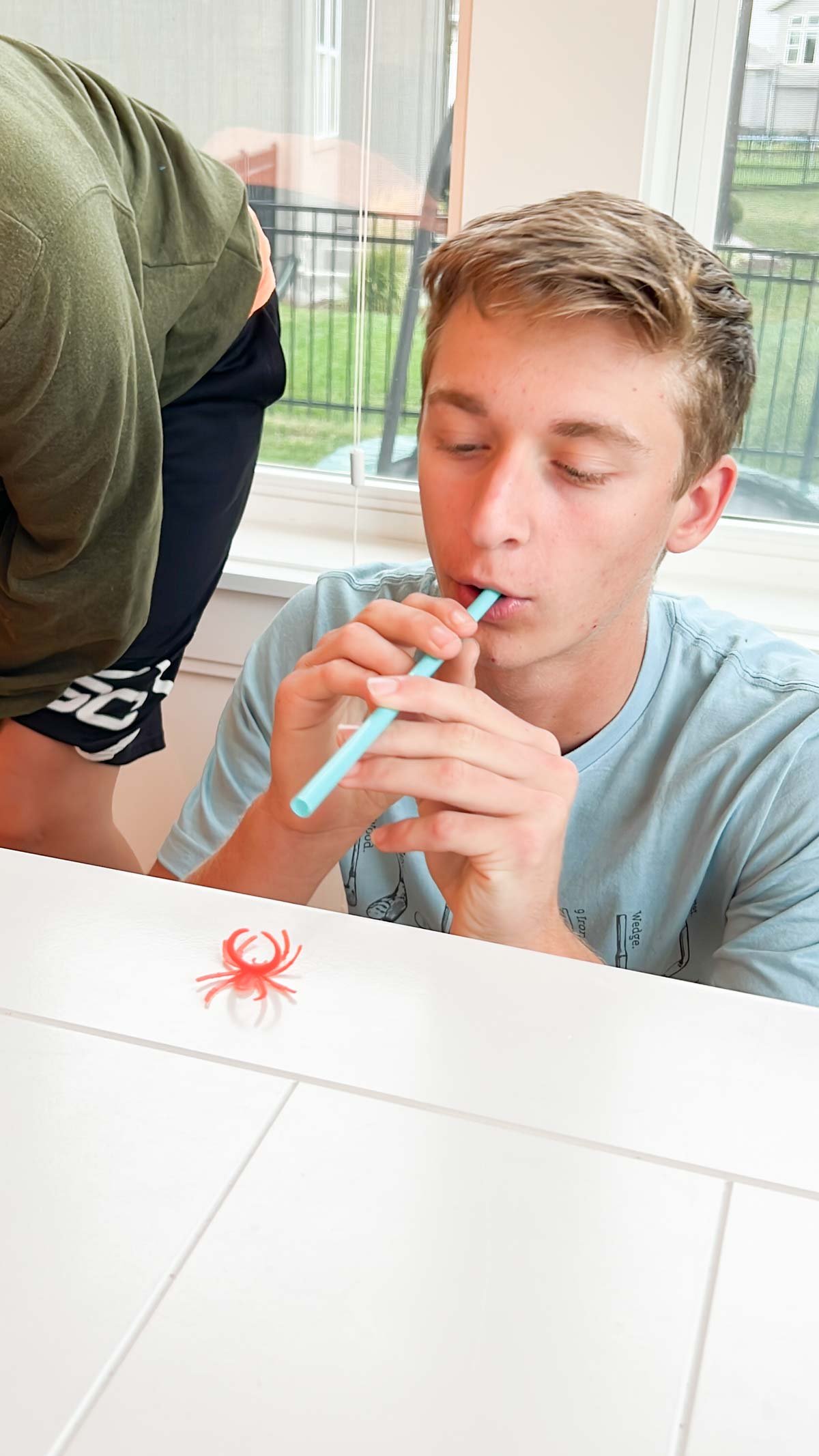 Teen blowing a plastic spider with a straw on a table