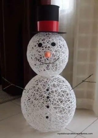 two DIY yarn balls stacks on top of each other with paper hat for a snowman