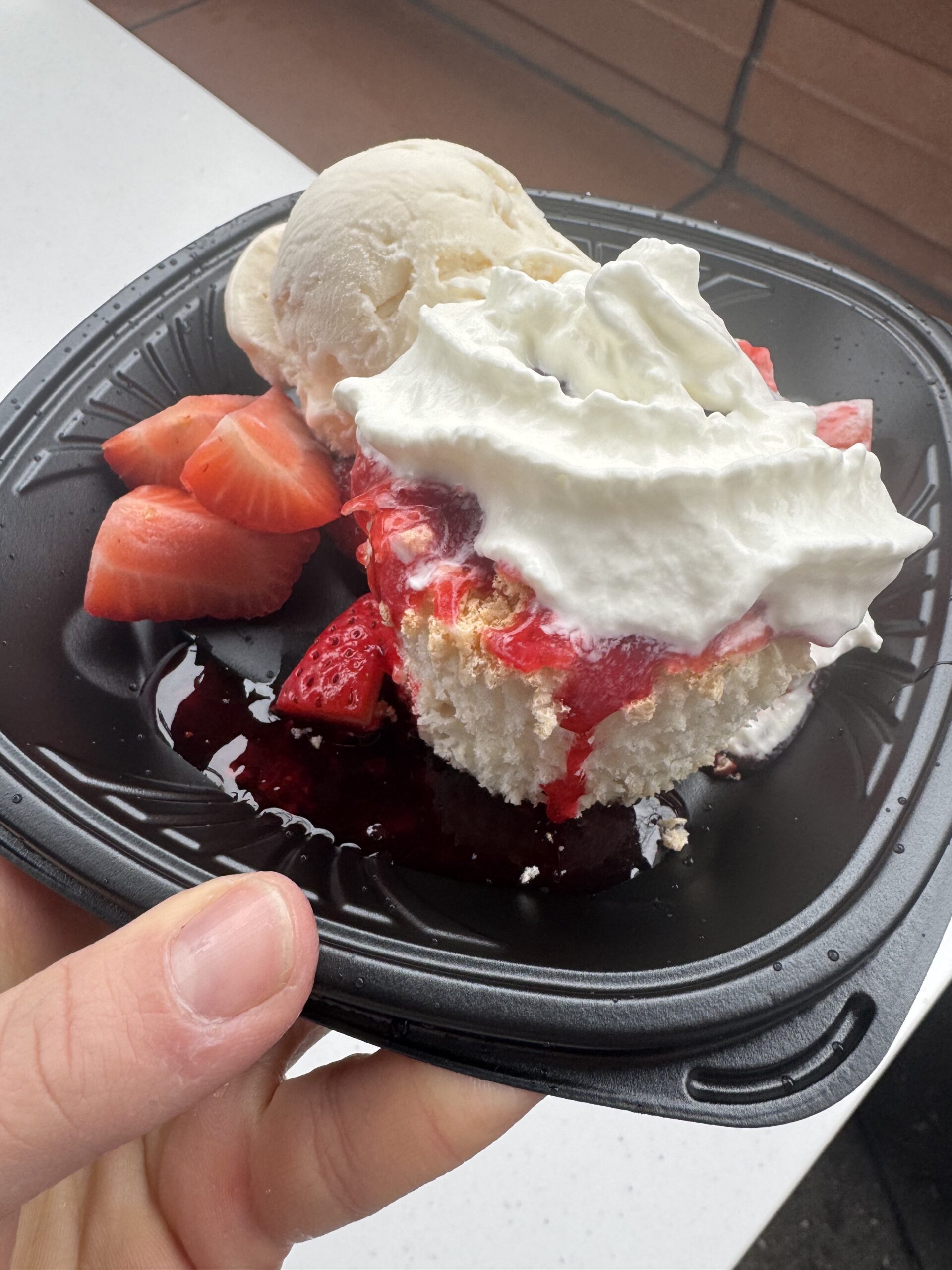 hand holding a black plate with a strawberry shortcake on it