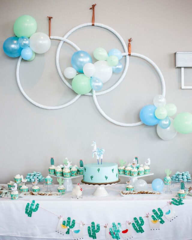 teal, blue, green, and white decorated dessert table with cactus cake and various llamas