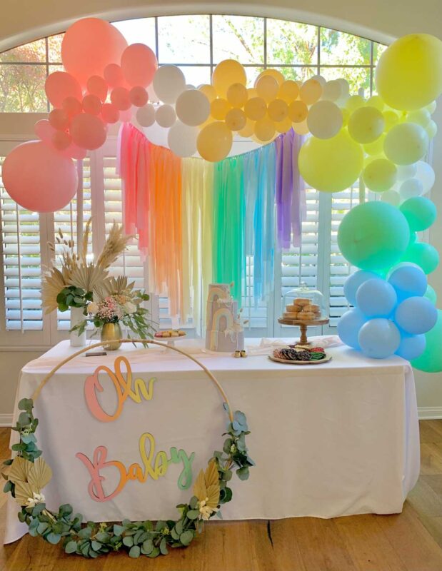rainbow balloon arch with a cake and donuts on a food table
