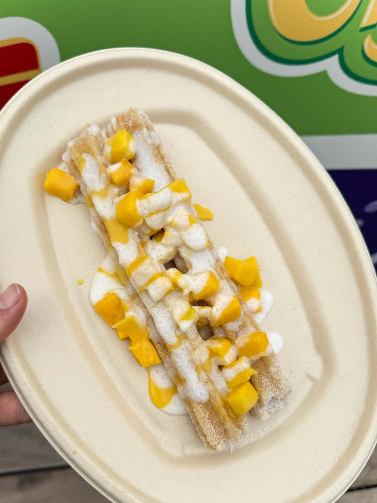 hand holding a plate with a mango sticky rice churro