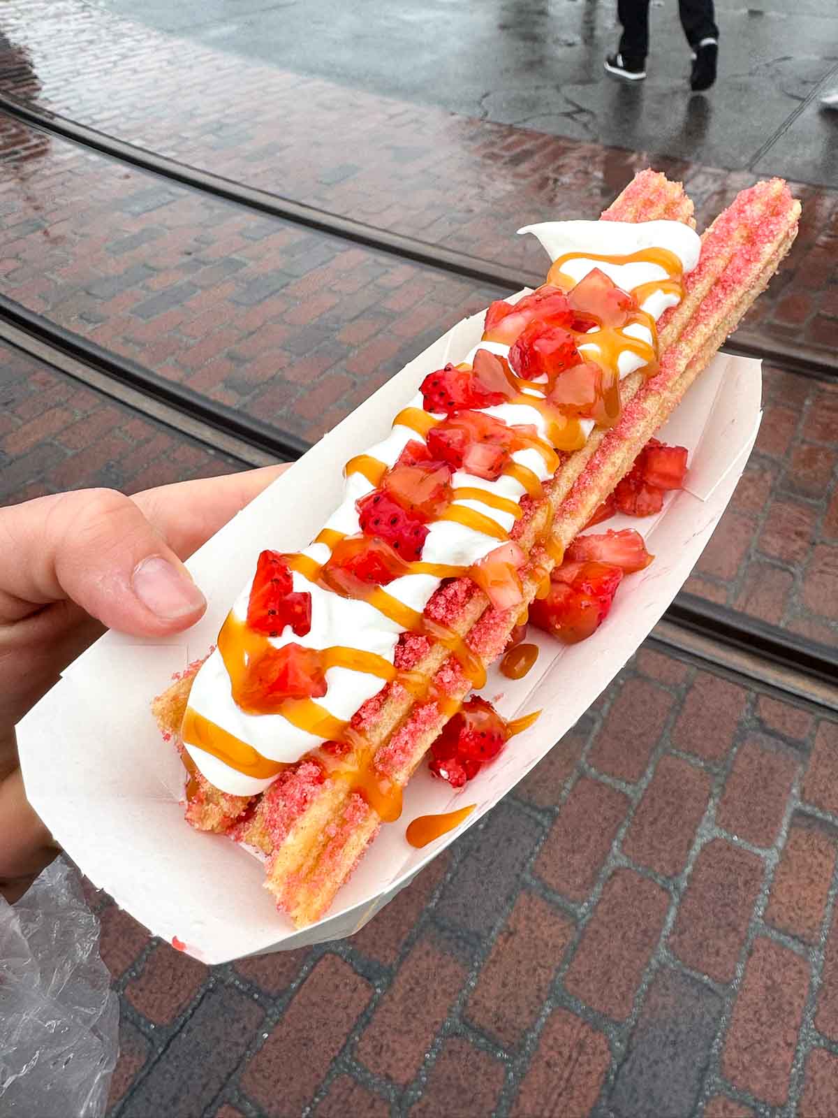 hand holding a plate with a strawberry caramel churro