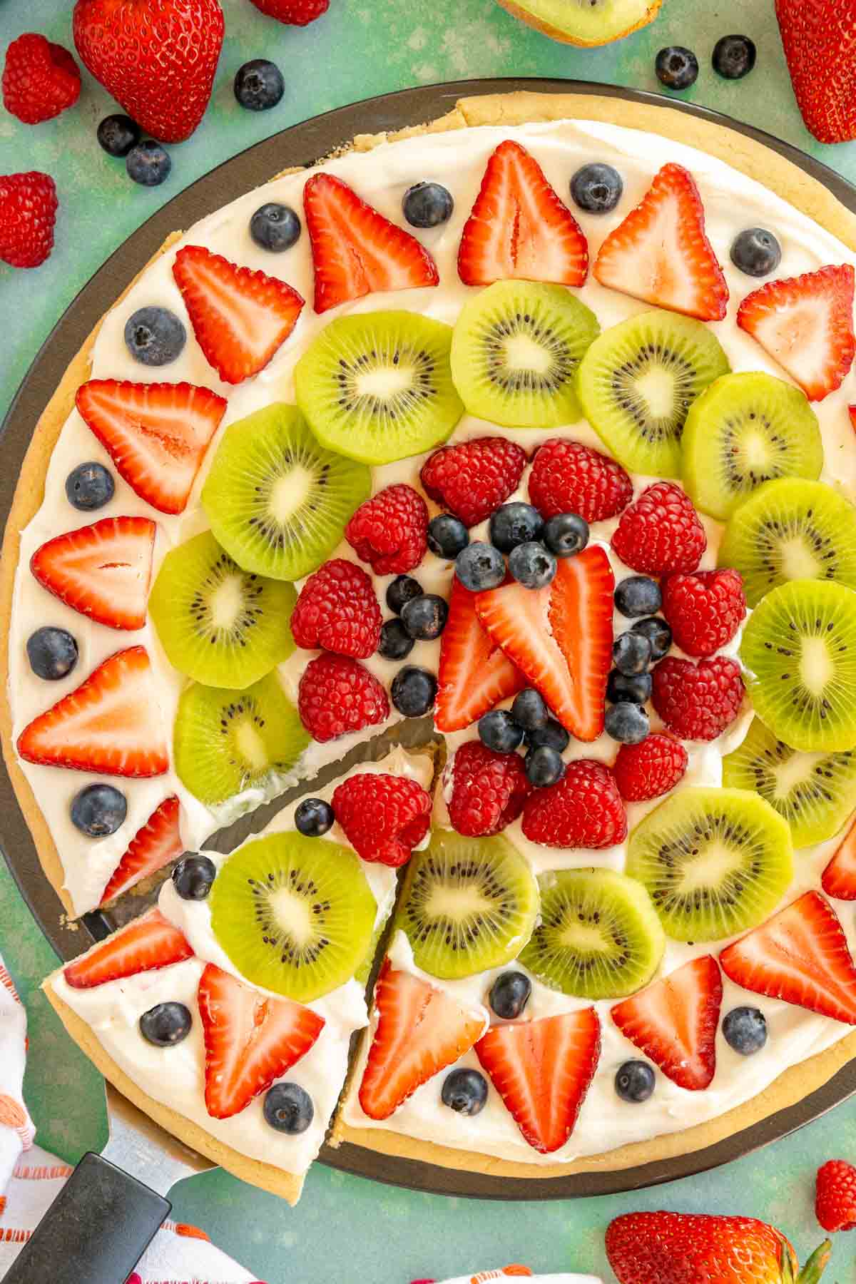 sugar cookie fruit pizza with a slice cut and pulled out on a spatula