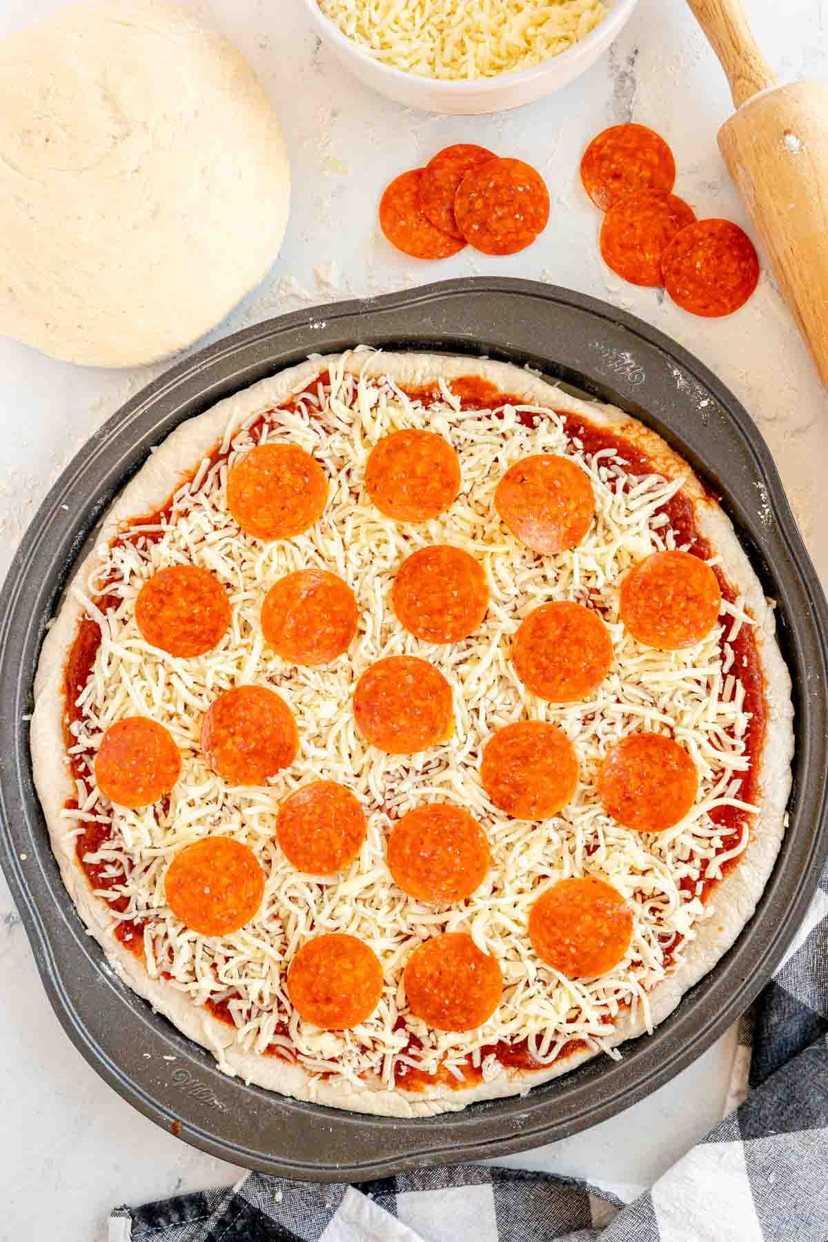 unbaked pizza dough topped with pepperoni and cheese on a pizza pan