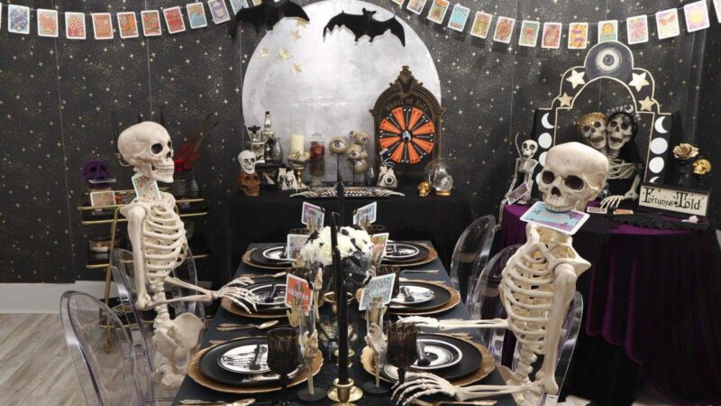 various skeletons sitting at a fortune teller themed dinner table with taro cards