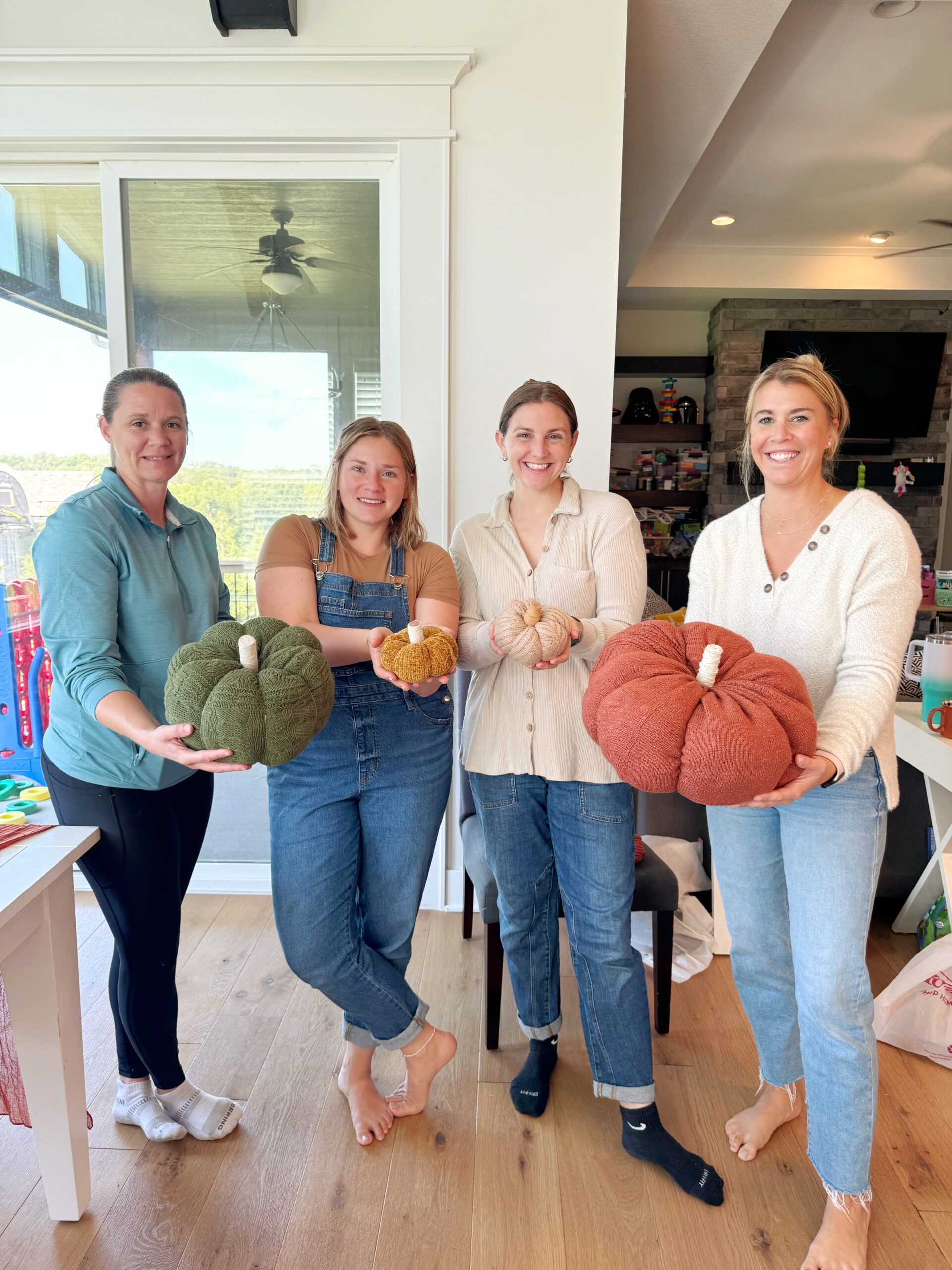 four women holding sweater pumpkins in their hands