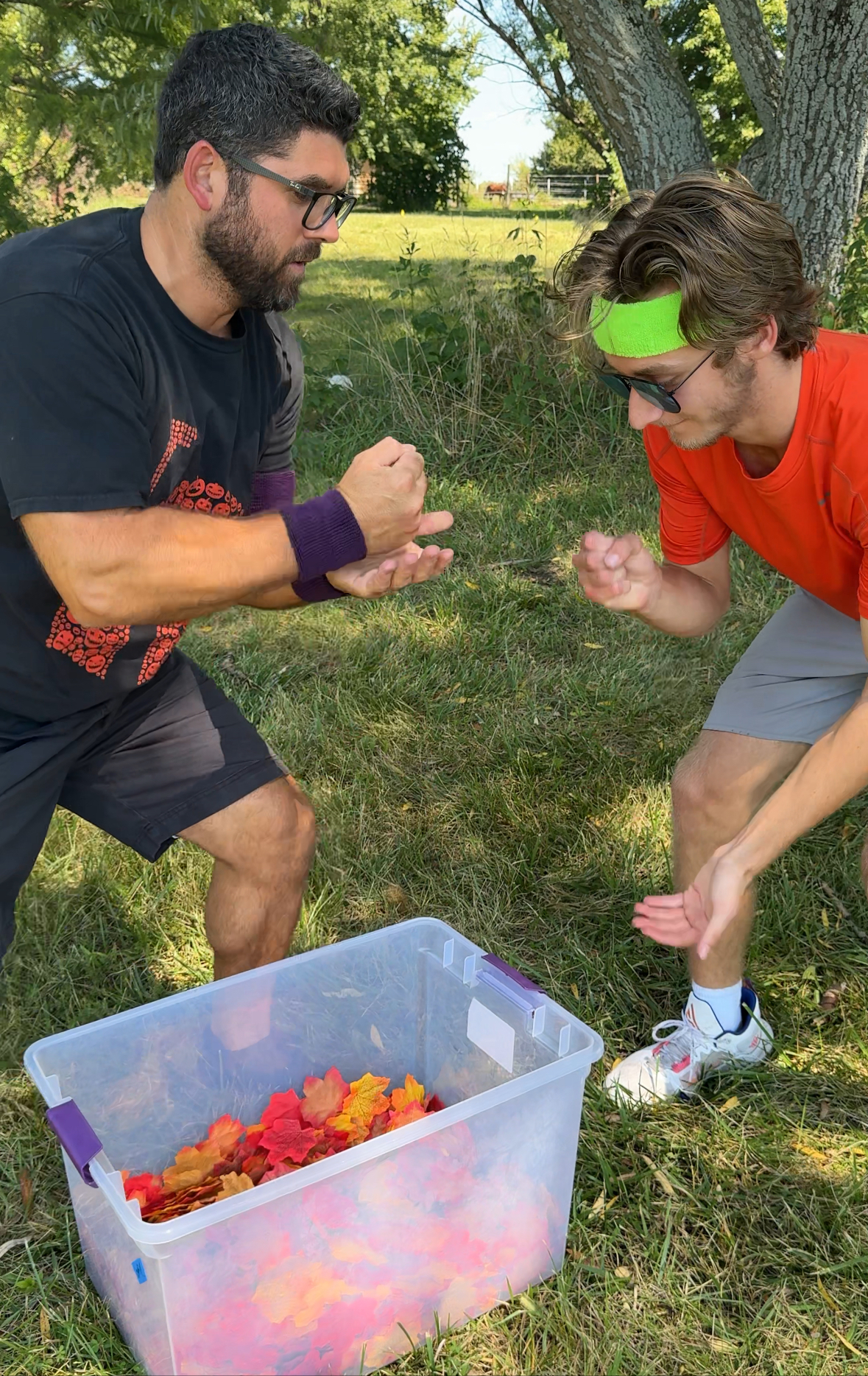 two men playing rock paper scissors over a bucket of leaves