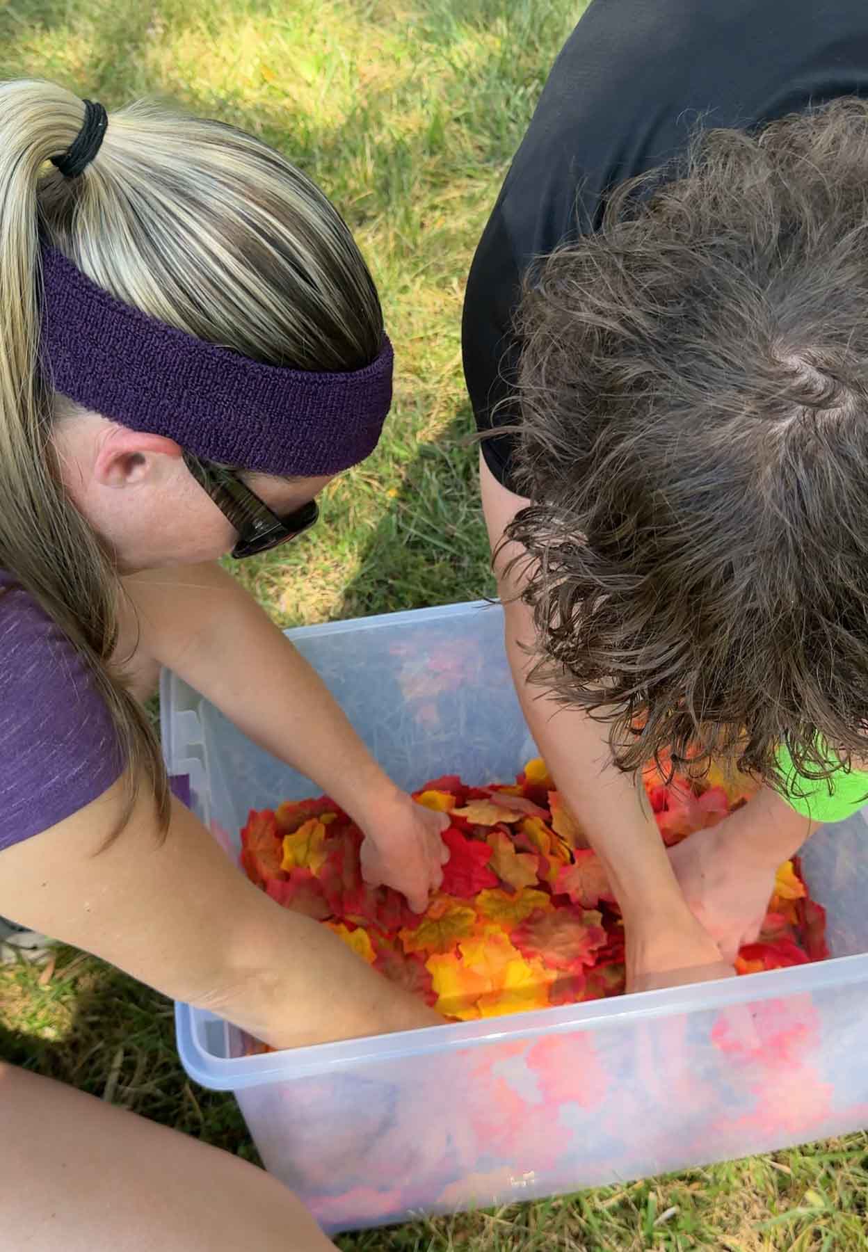 two people searching through a bucket of plastic leaves