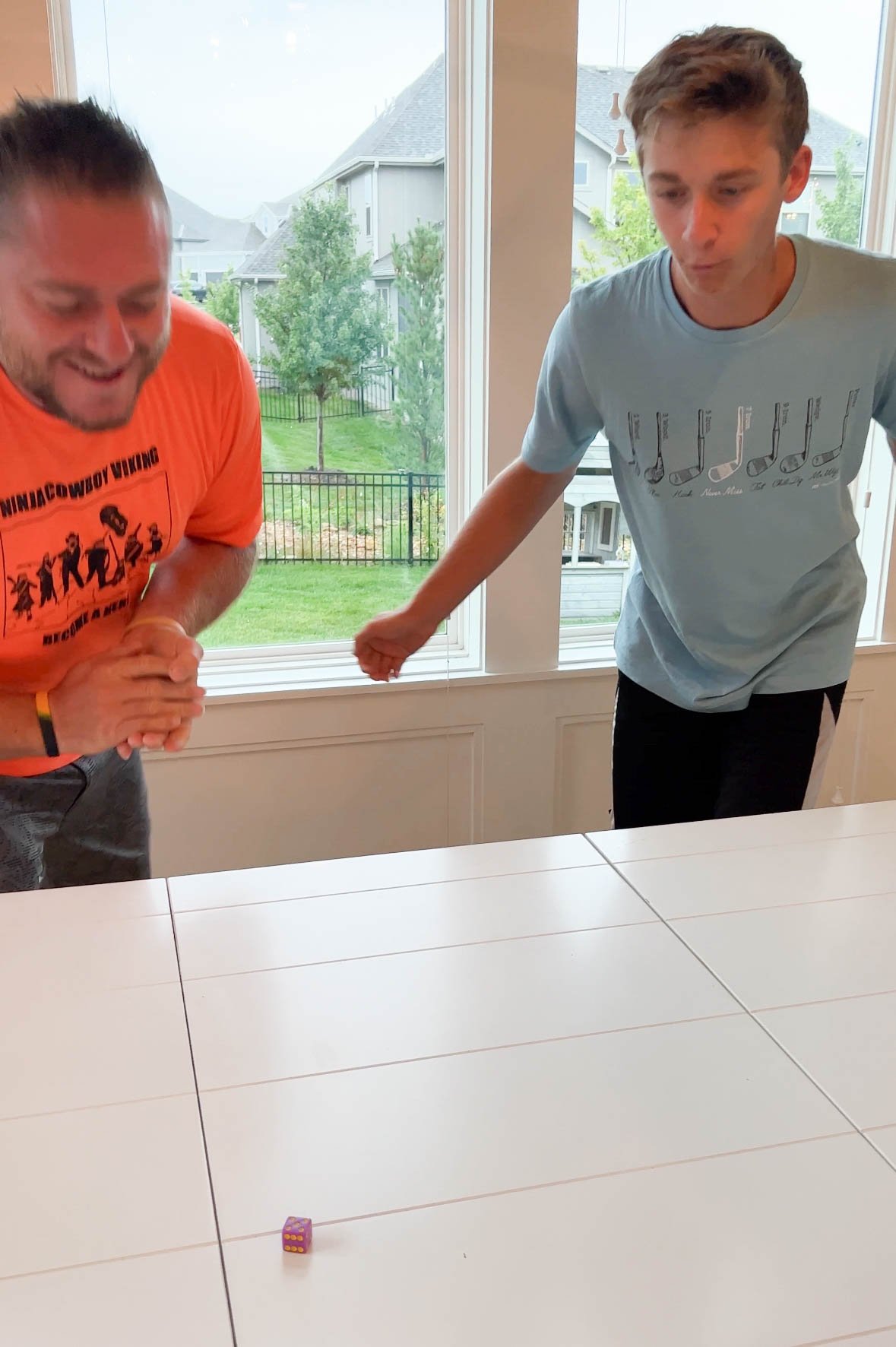 a teen boy and a man rolling dice on a white table