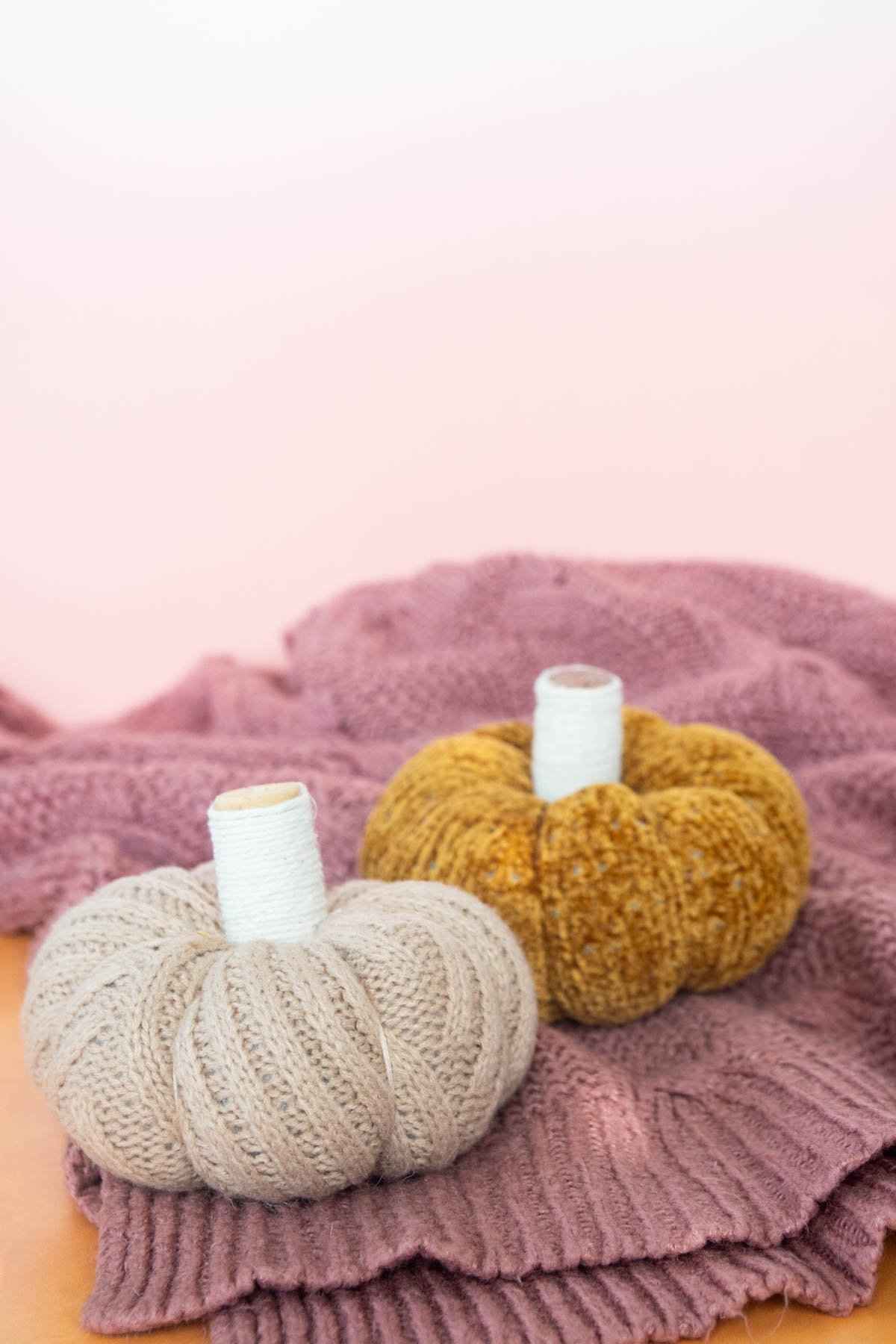 two small sweater pumpkins with a pink sweater in the background