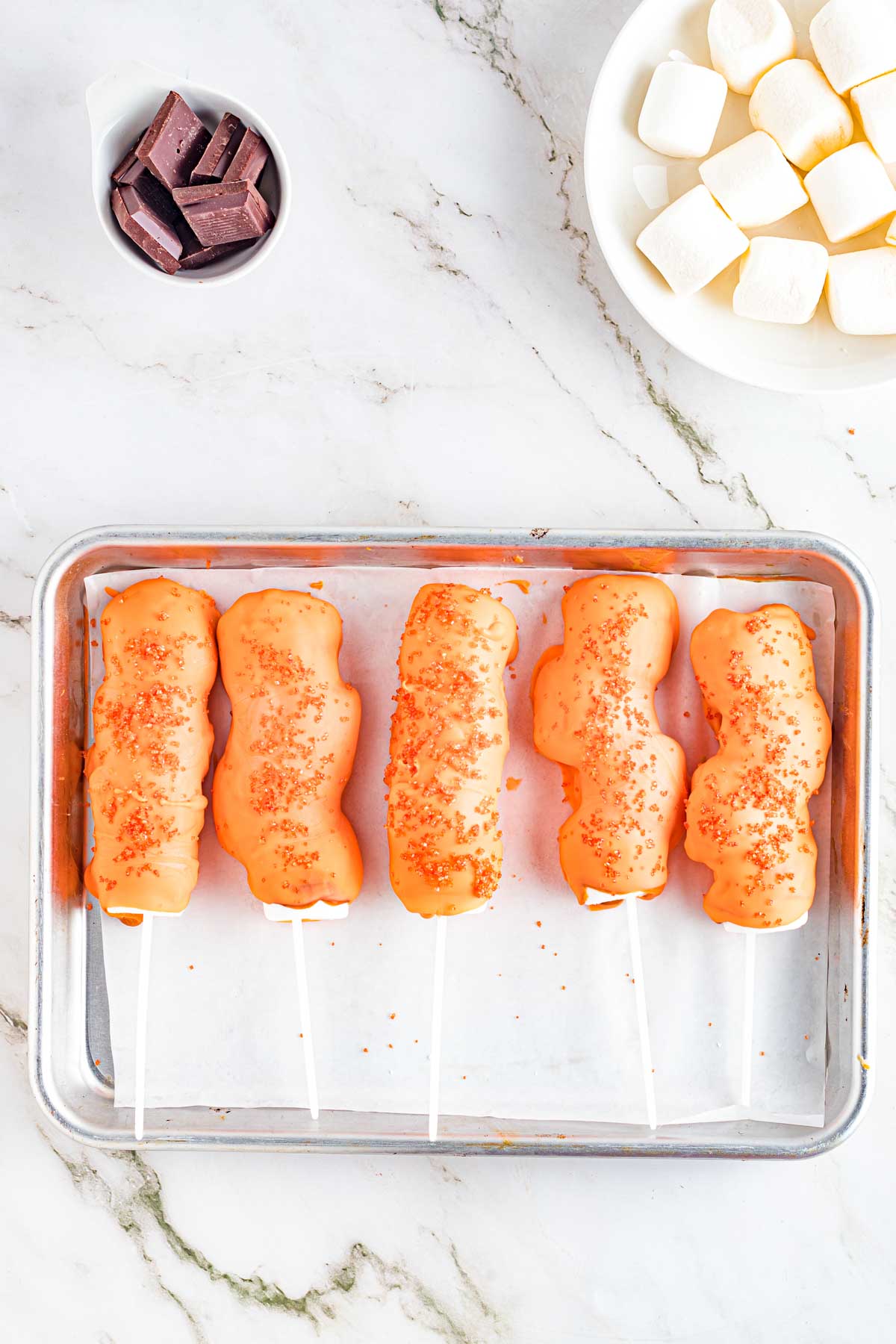 baking sheet with orange chocolate covered marshmallows on lollipop sticks