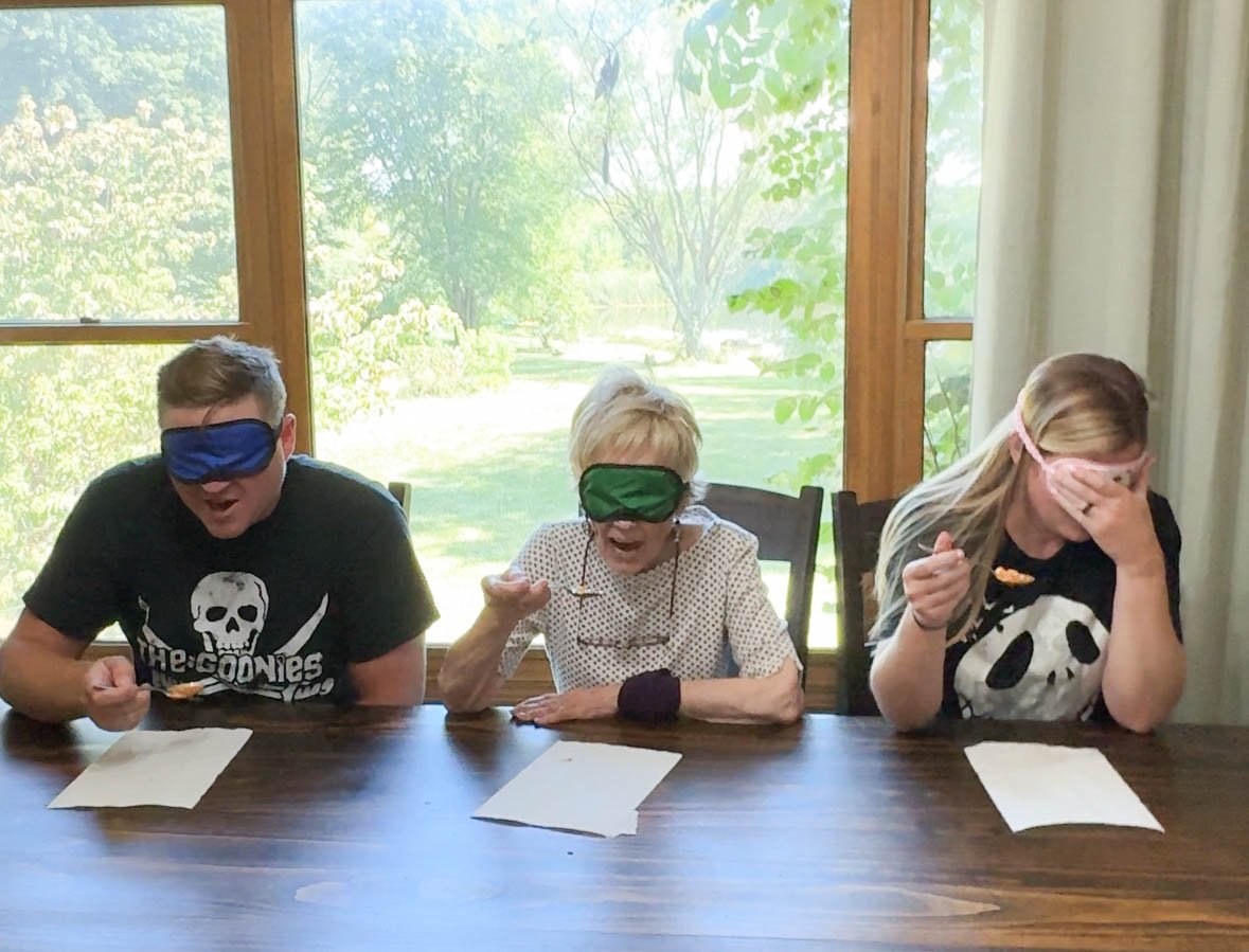 three people with blindfolds on eating food 