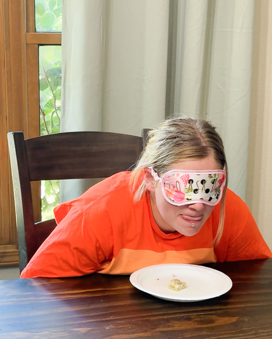 woman with a blindfold on and orange shirt playing a Halloween guess the food game