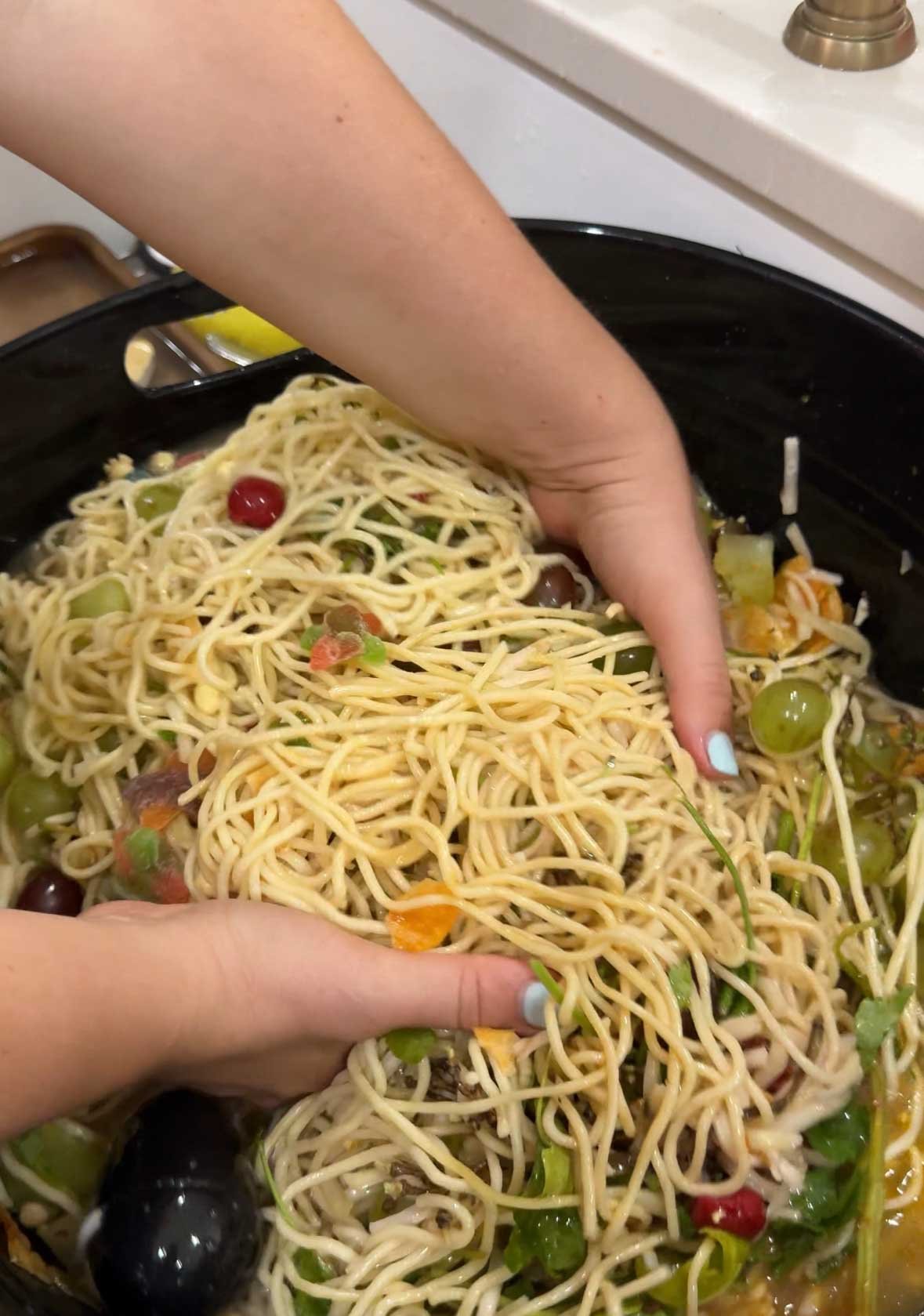 woman's hands holding a bunch of noodles and other food in a cauldron