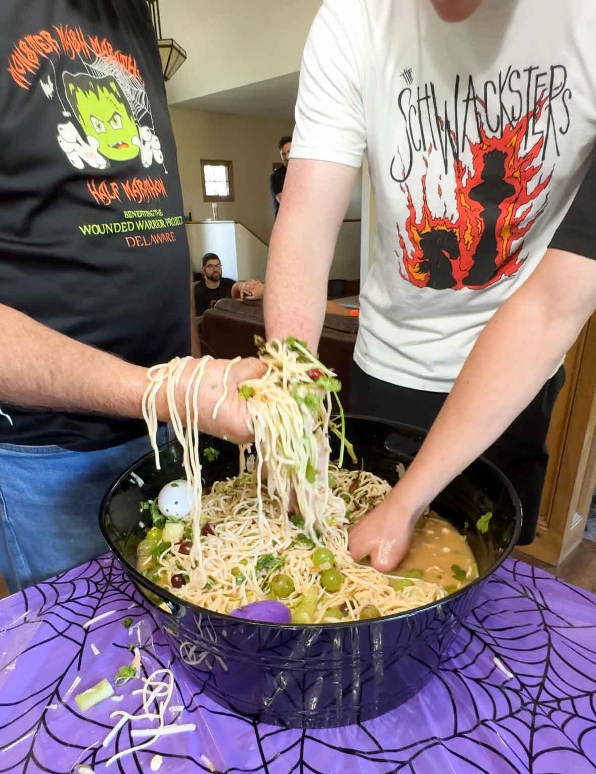 three men holding noodles above a cauldron