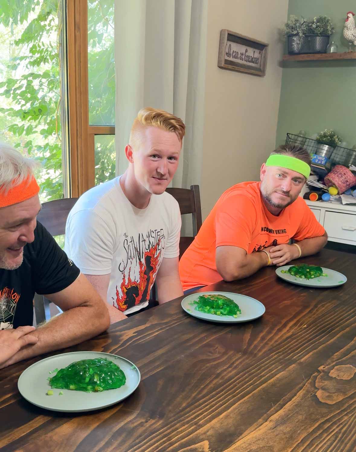 three men sitting at a table with green jello on a plate in front of them