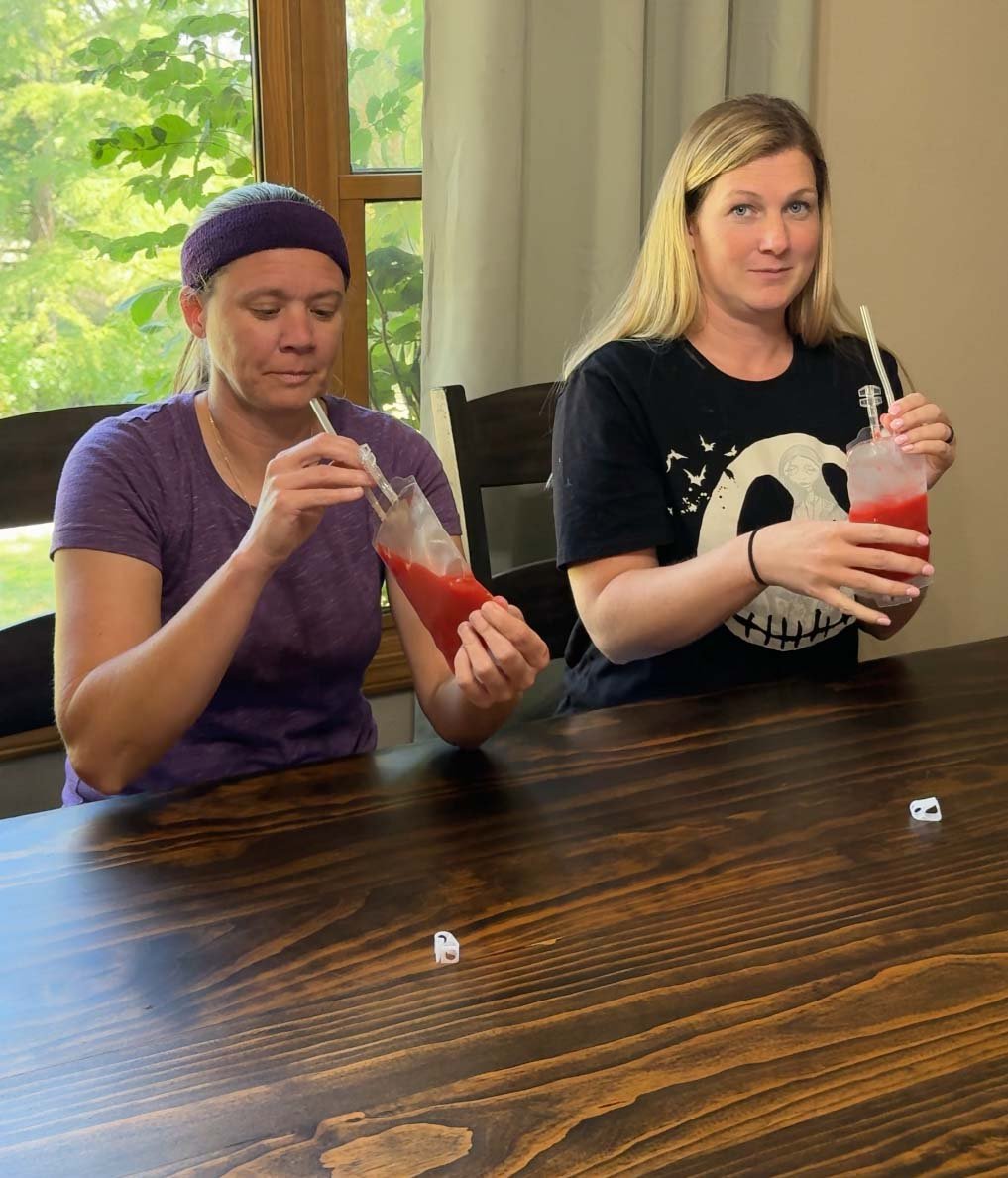 two women holding blood bags filled with tomato juice