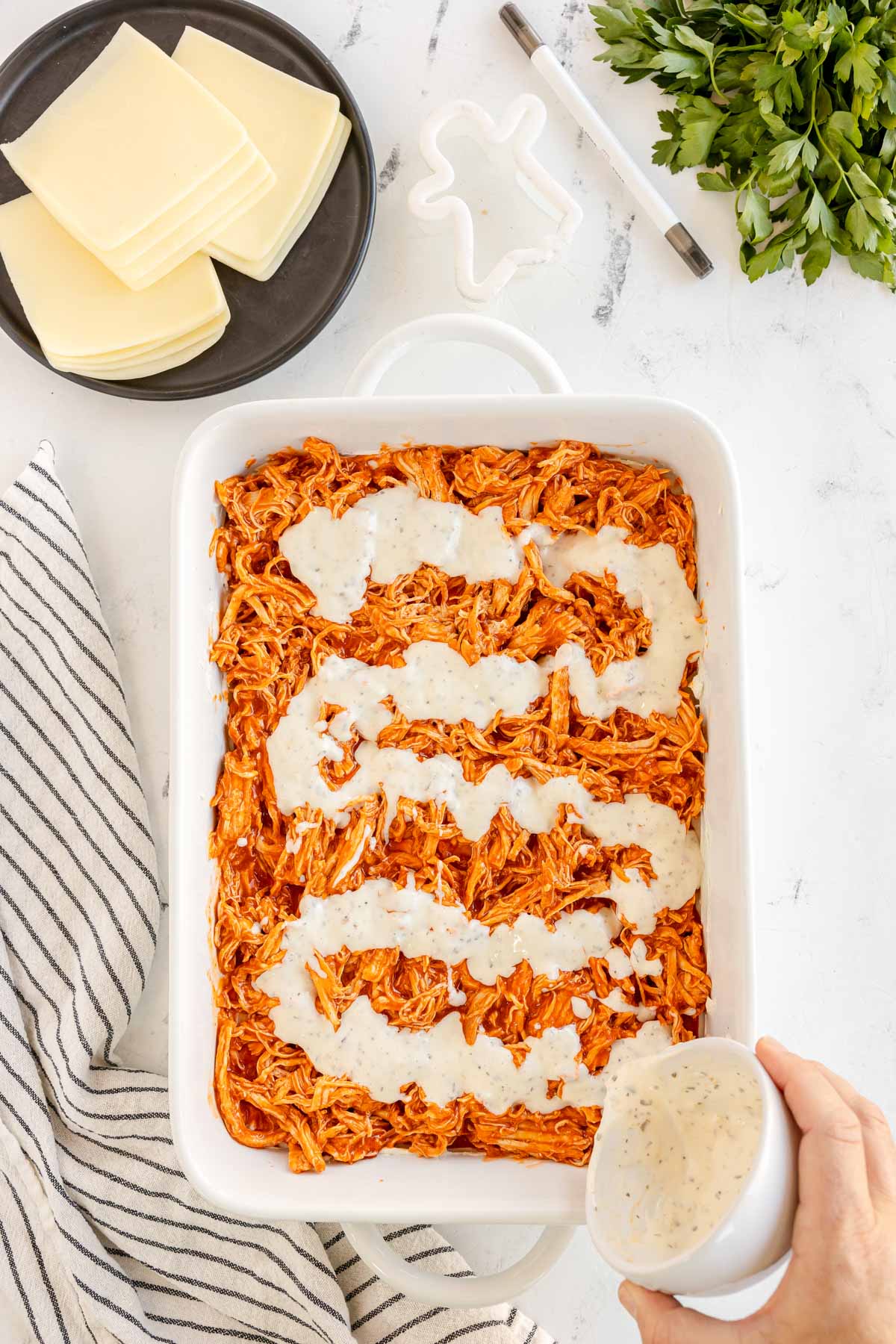 cup pouring ranch dressing on top of buffalo chicken dip