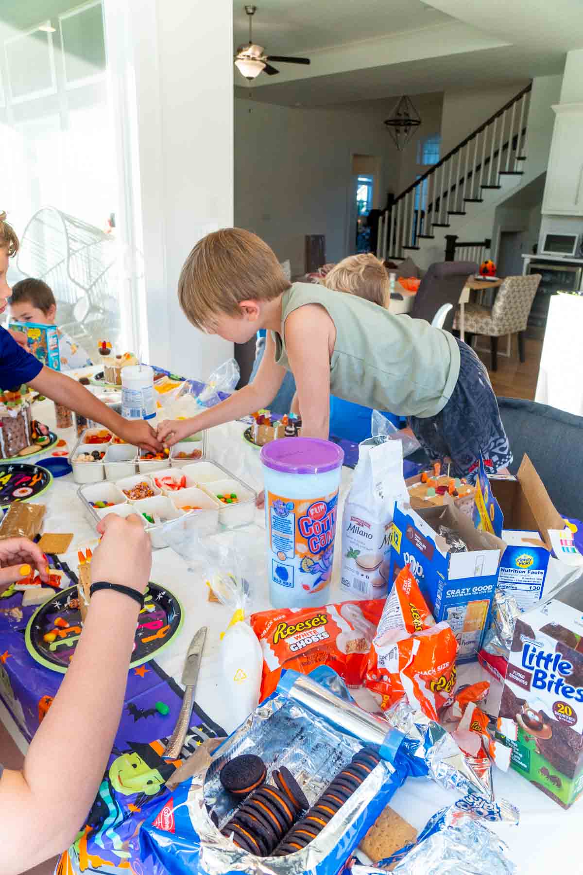 kids making Halloween gingerbread houses on a plastic tablecloth