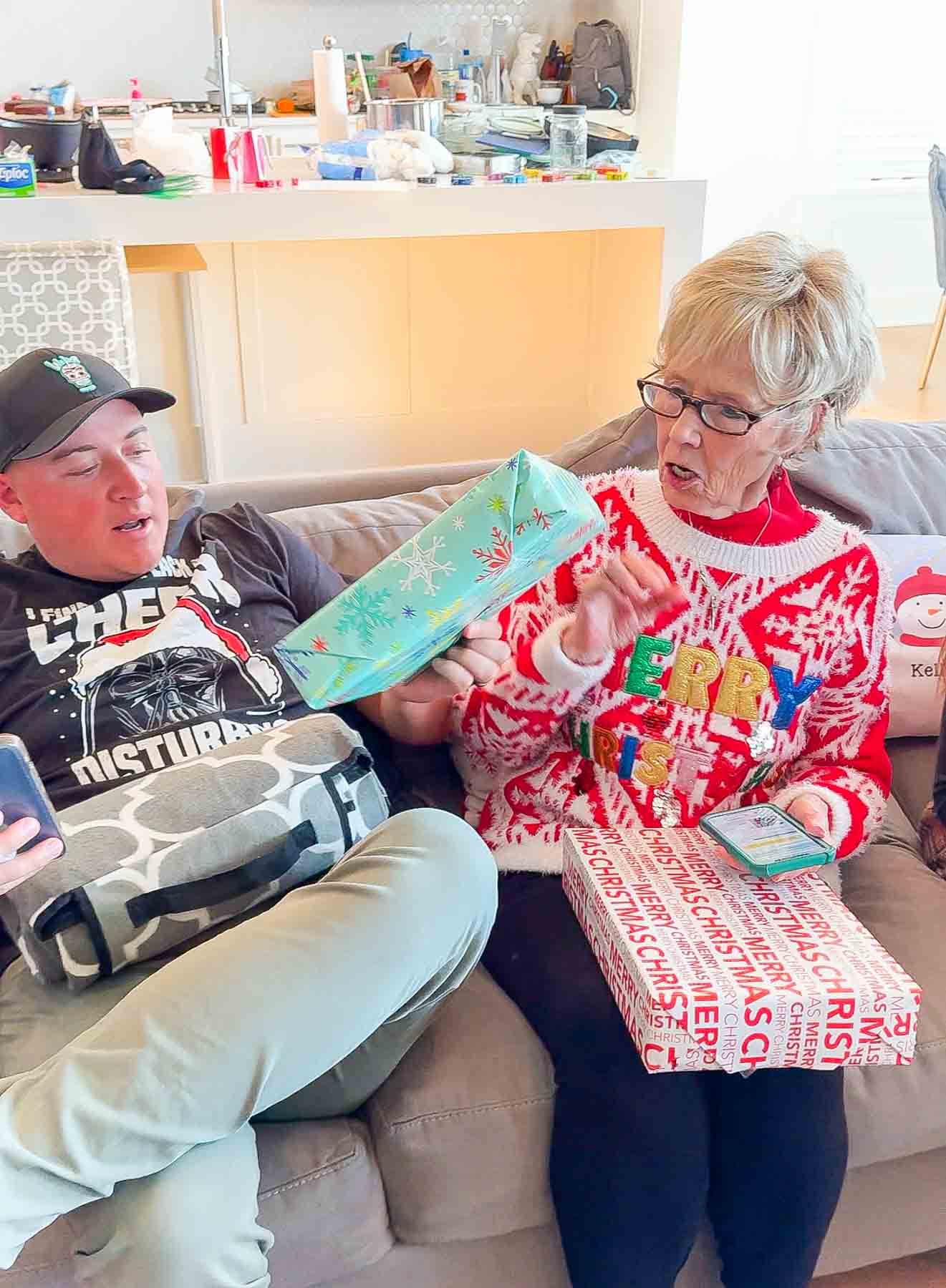 a man passing a gift to a grandma on a couch