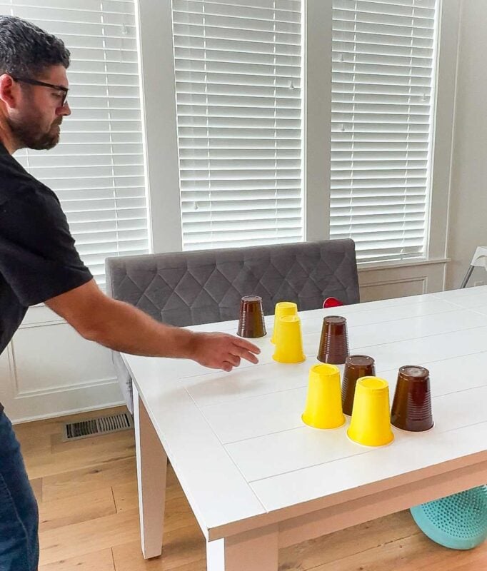 man holding his hand out toward yellow and brown cups on a table