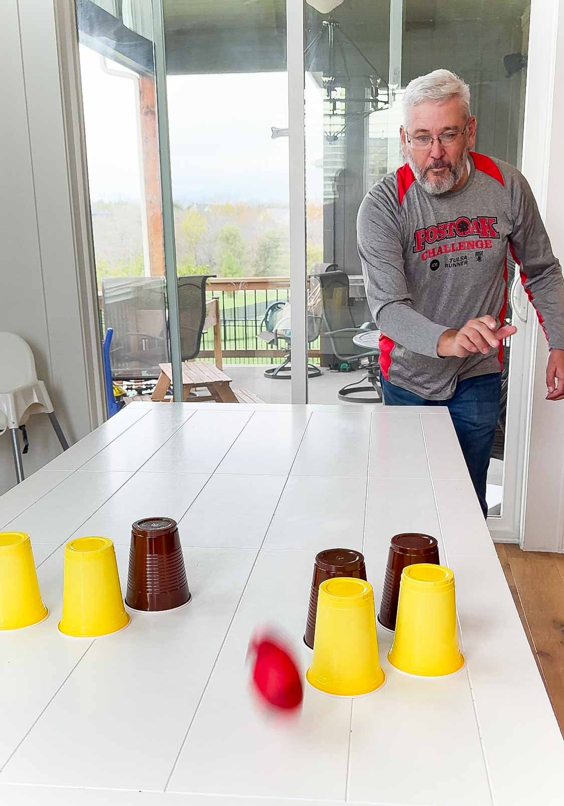 Man throwing a football at yellow and brown cups on a table