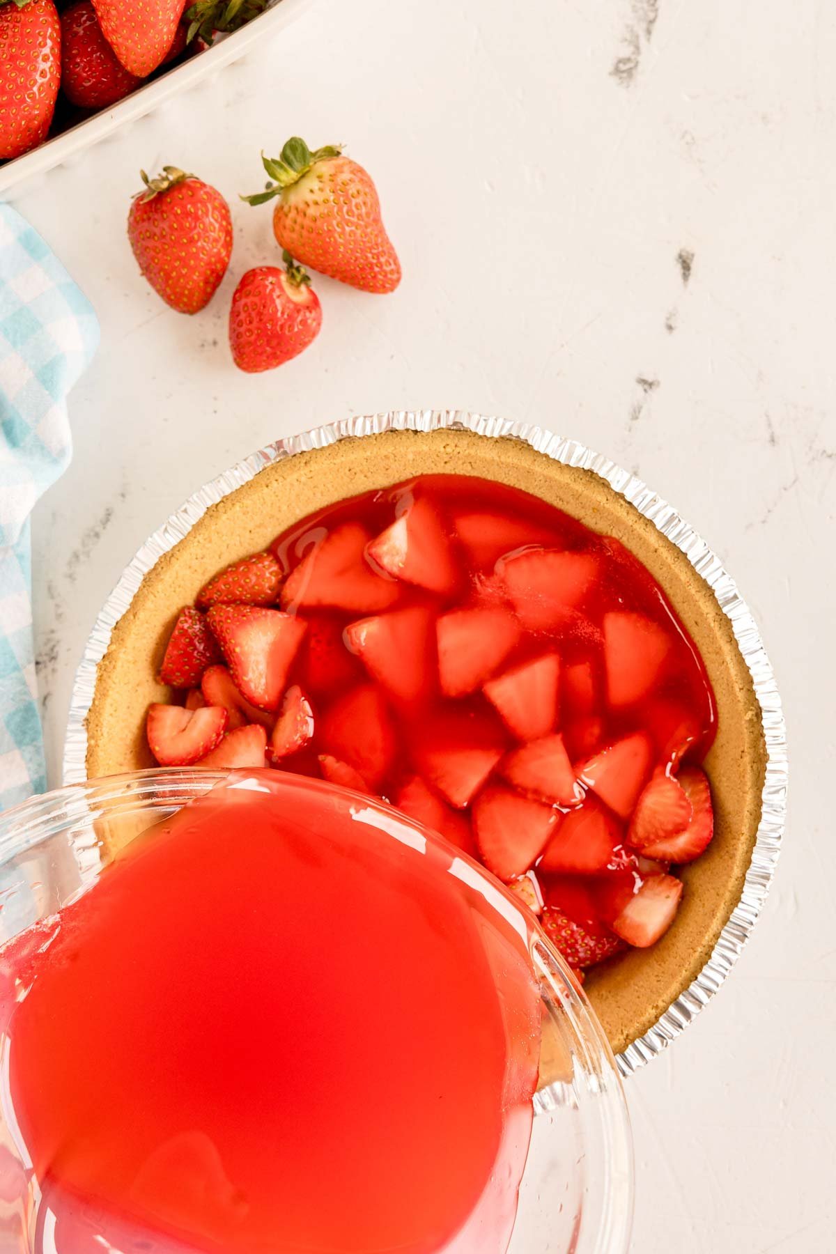 pouring jello mixture over top of sliced strawberries 