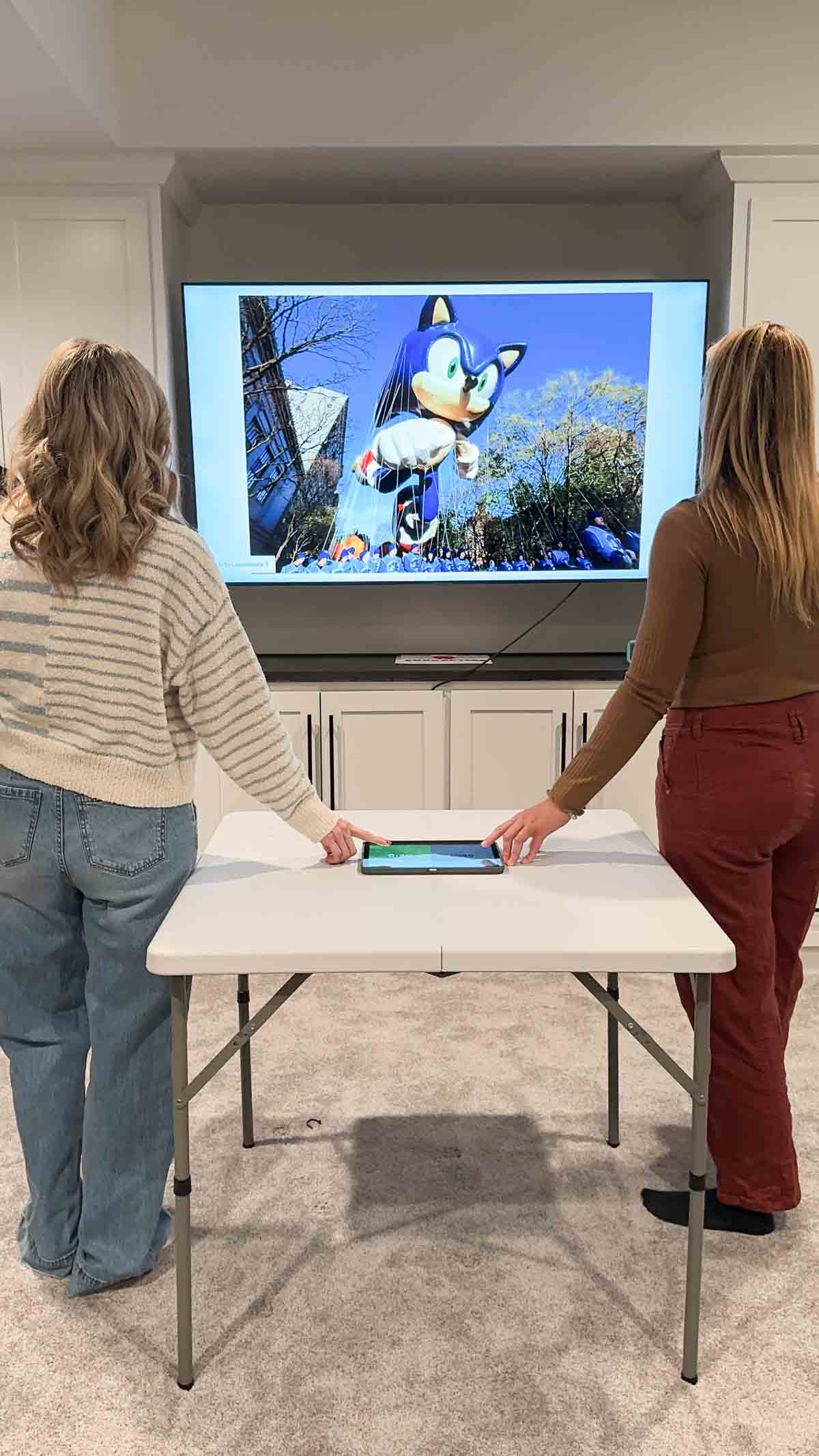 two women standing at a table looking at a TV screen 