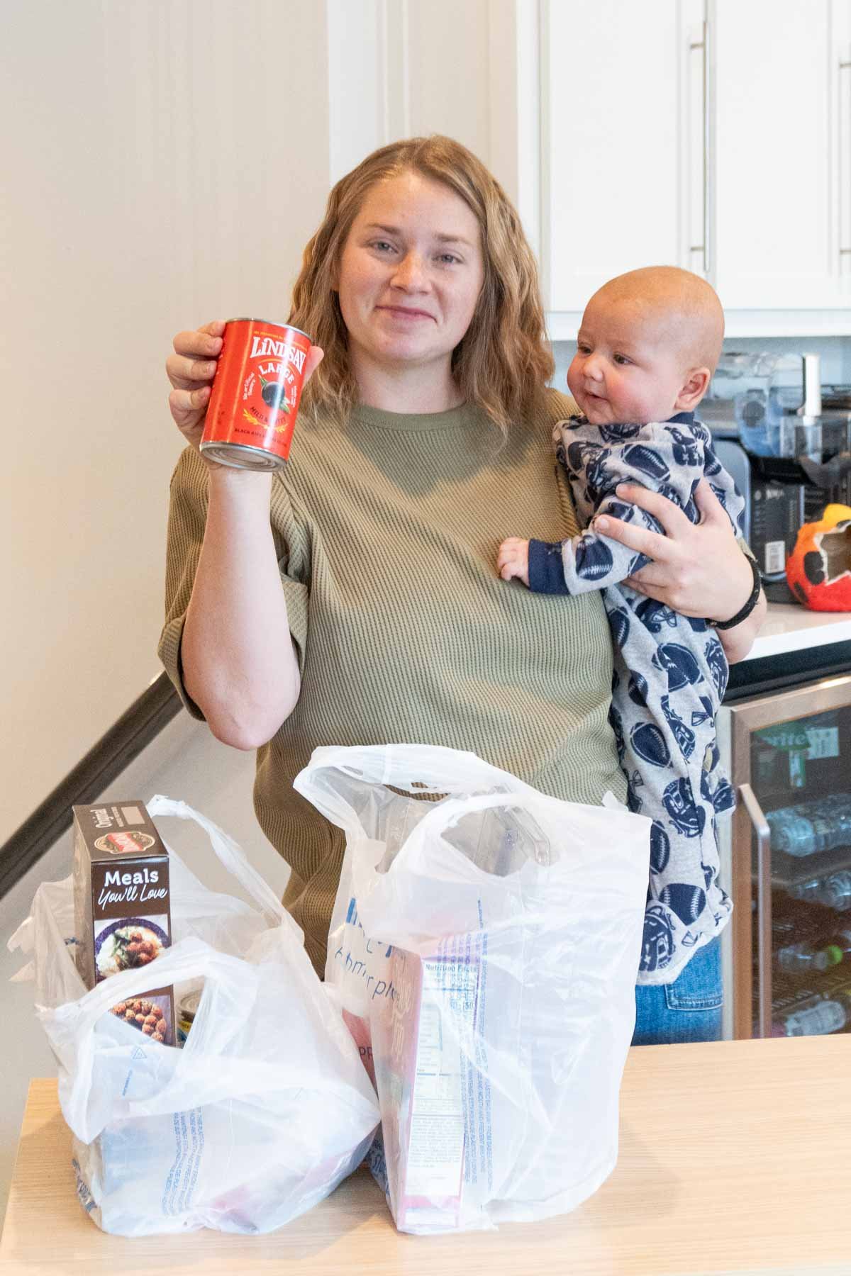 woman holding a baby and a can of black olives