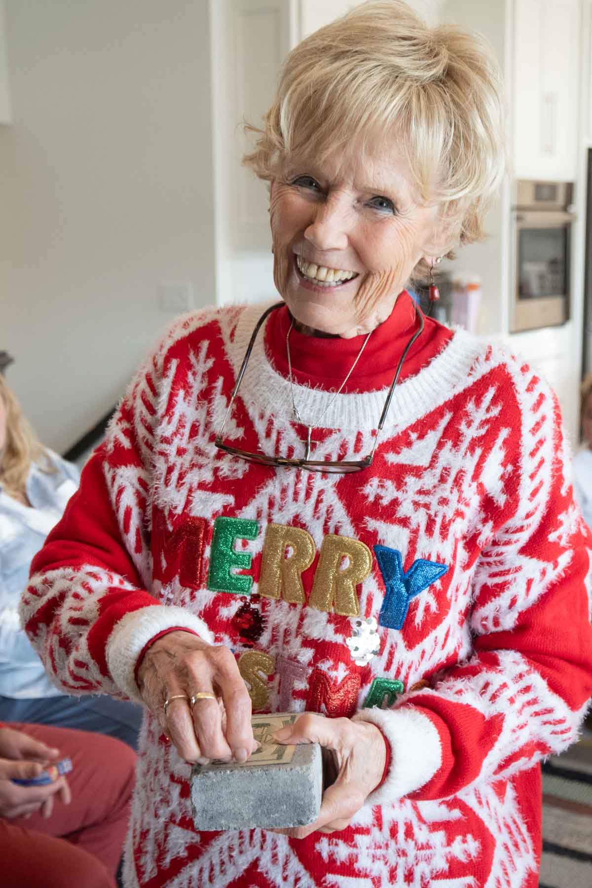 grandma in a Christmas sweater holding a brick with cash inside