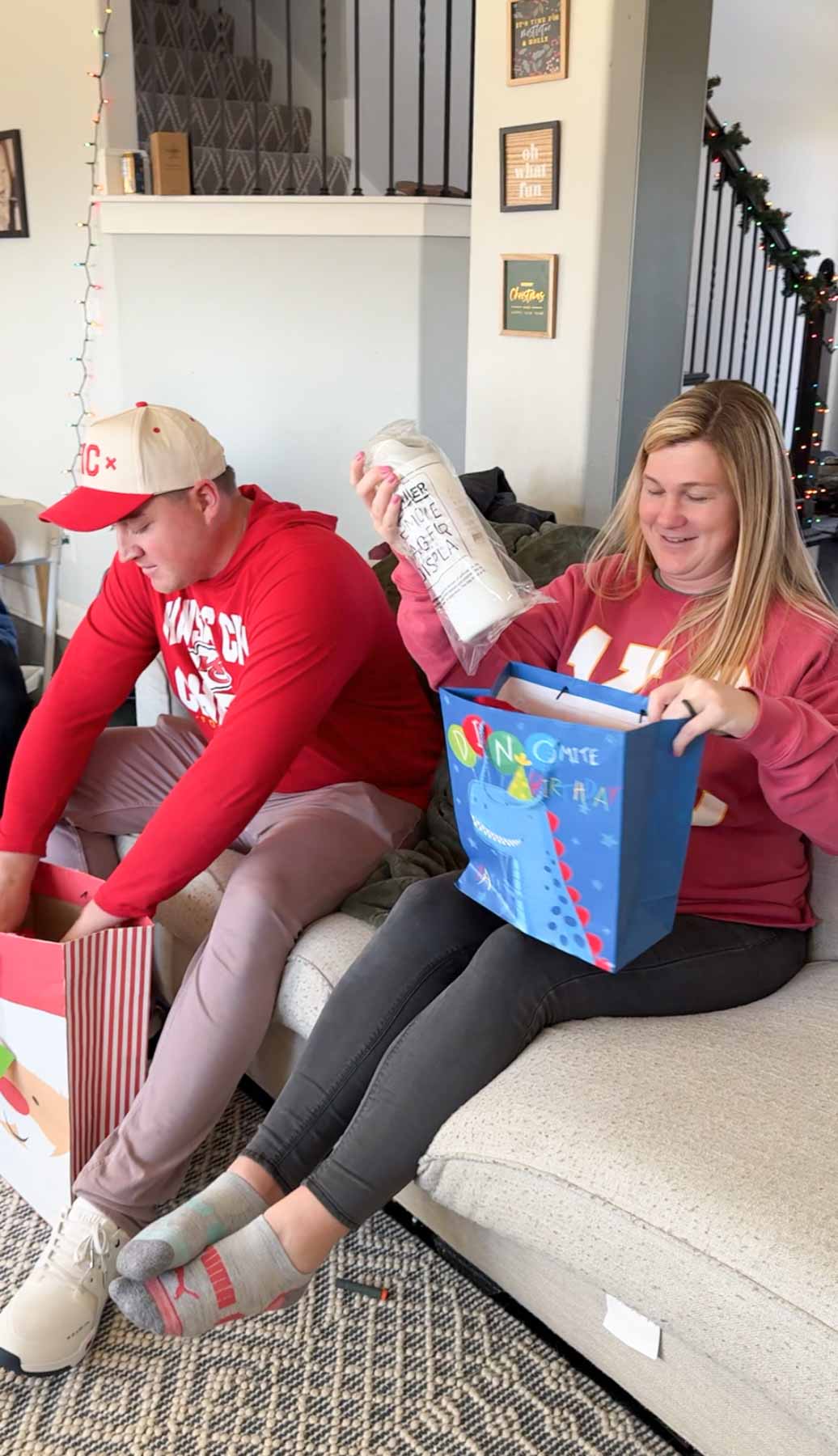 a man and a woman sitting on a couch unwrapping gifts