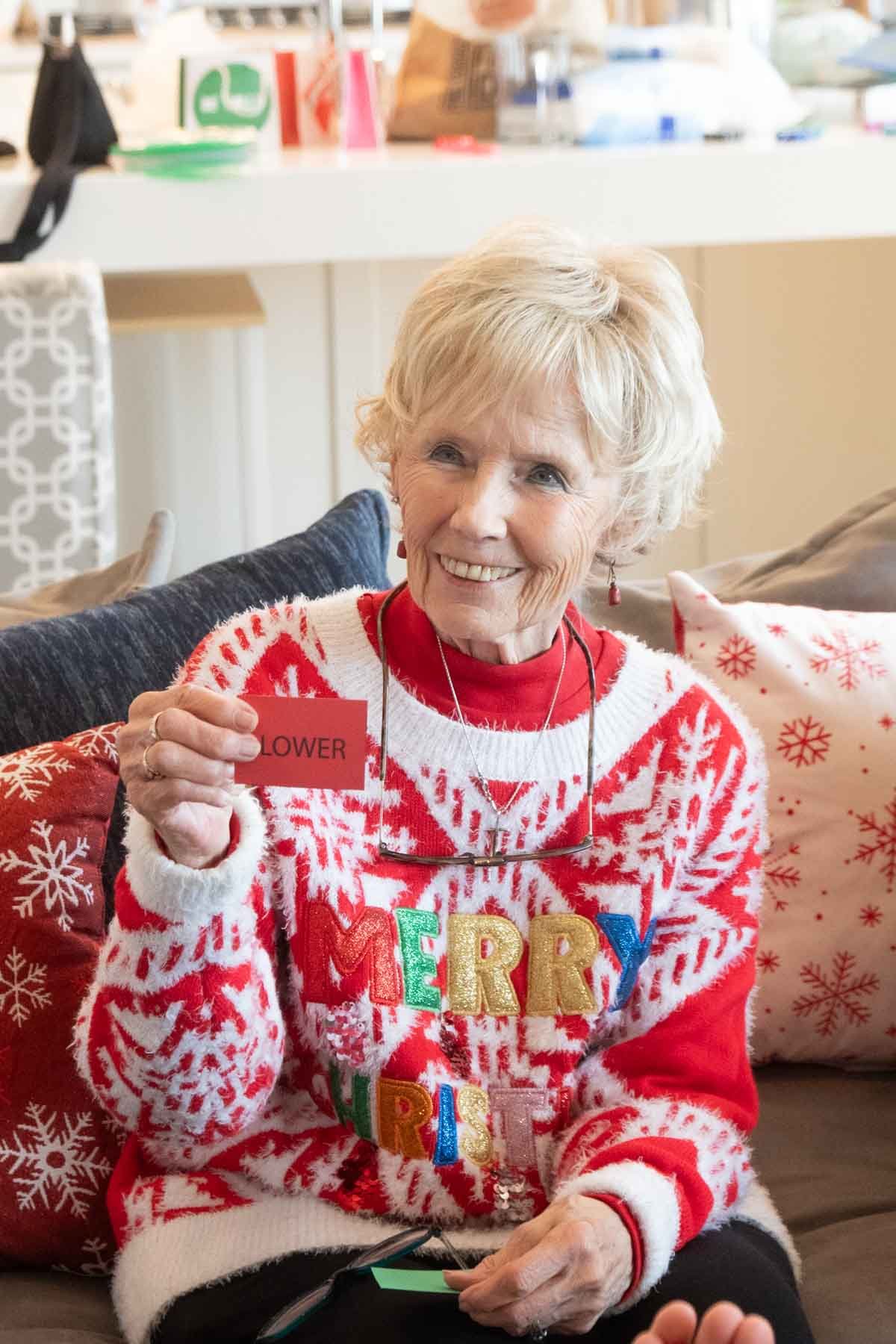 grandma in a christmas sweater holding a lower card