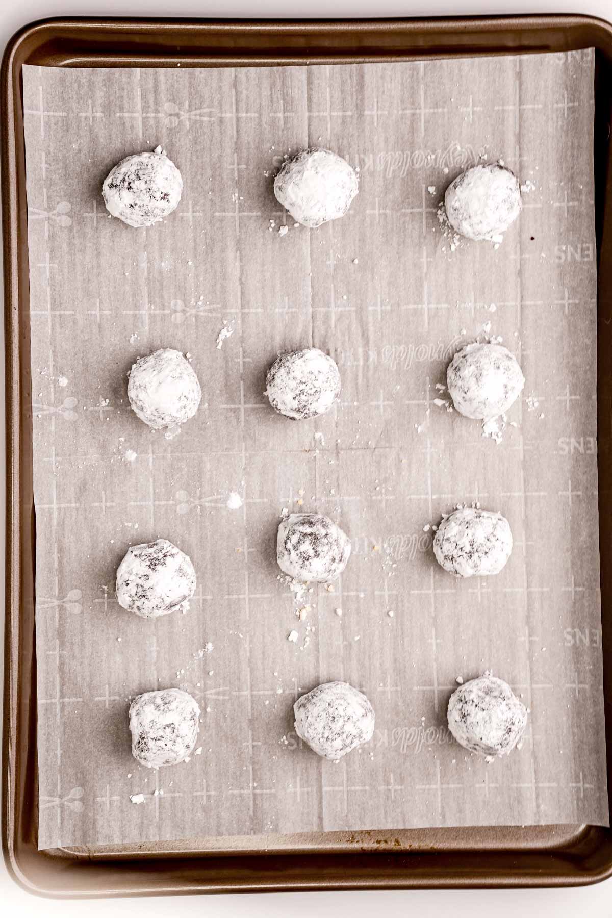 chocolate cookie dough balls rolled in powdered sugar on a baking sheet