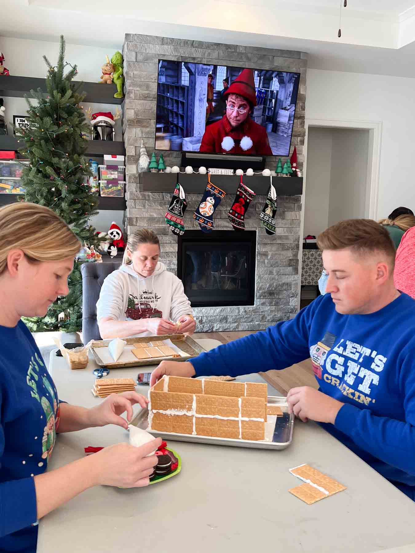 couple in blue sweatshirts making gingerbread houses