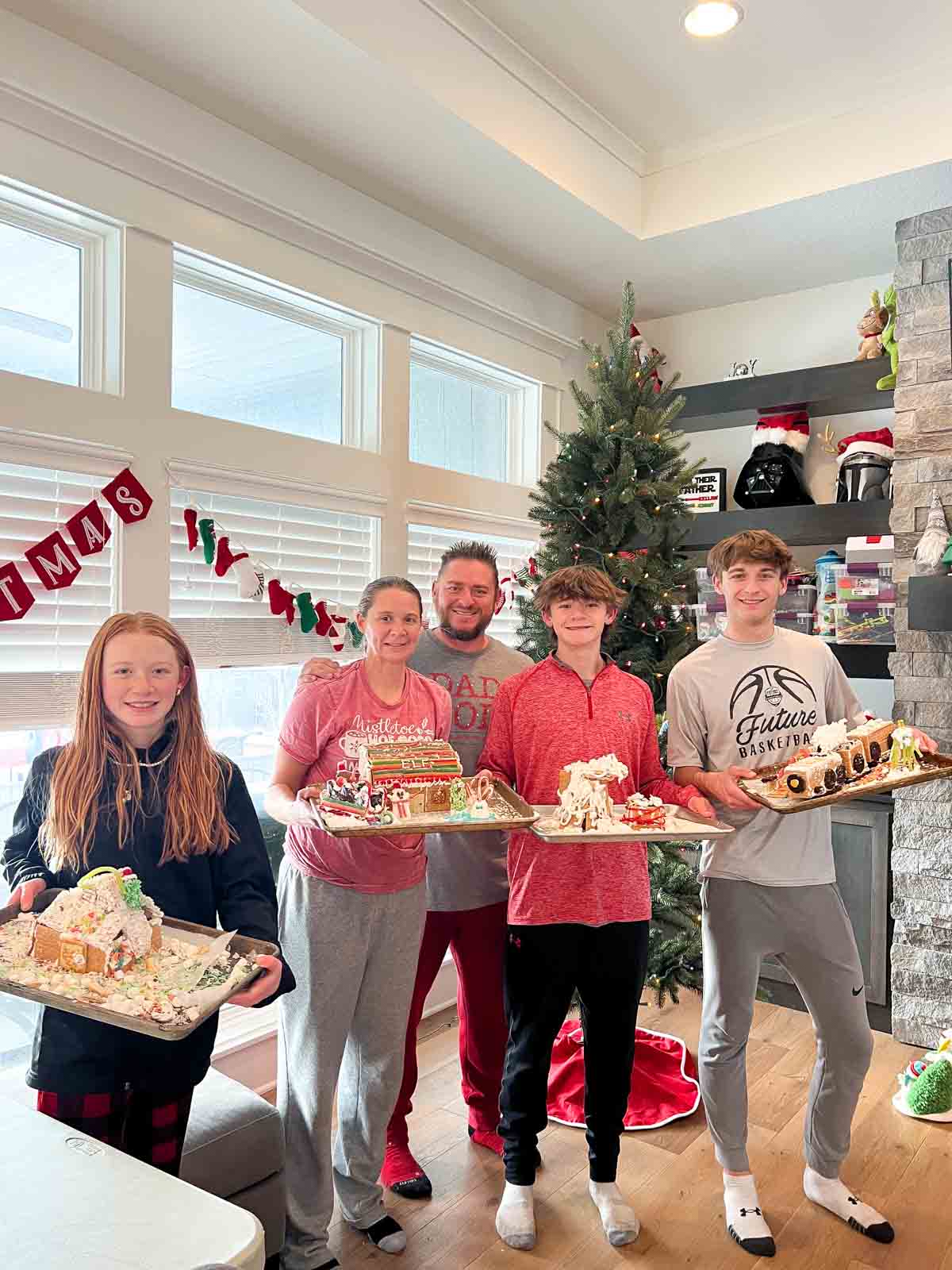 family holding baking sheets with gingerbread houses on them