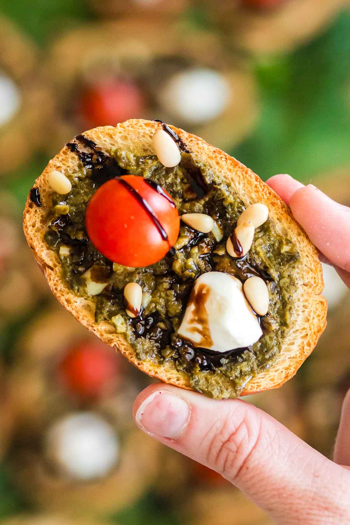 hand holding a pesto crostini with cheese