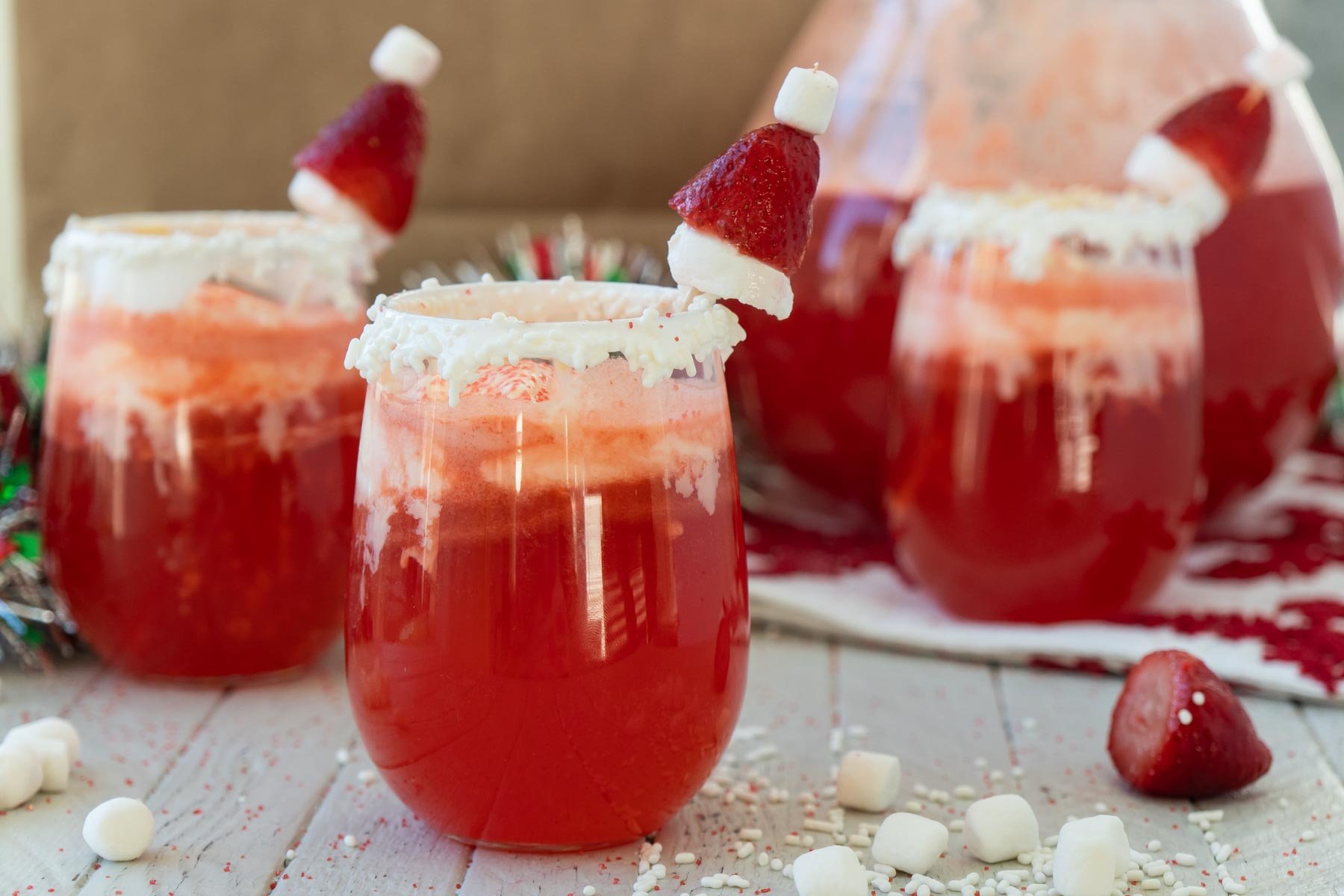 three glasses of red Santa Claus punch with strawberry Santa hats on top 