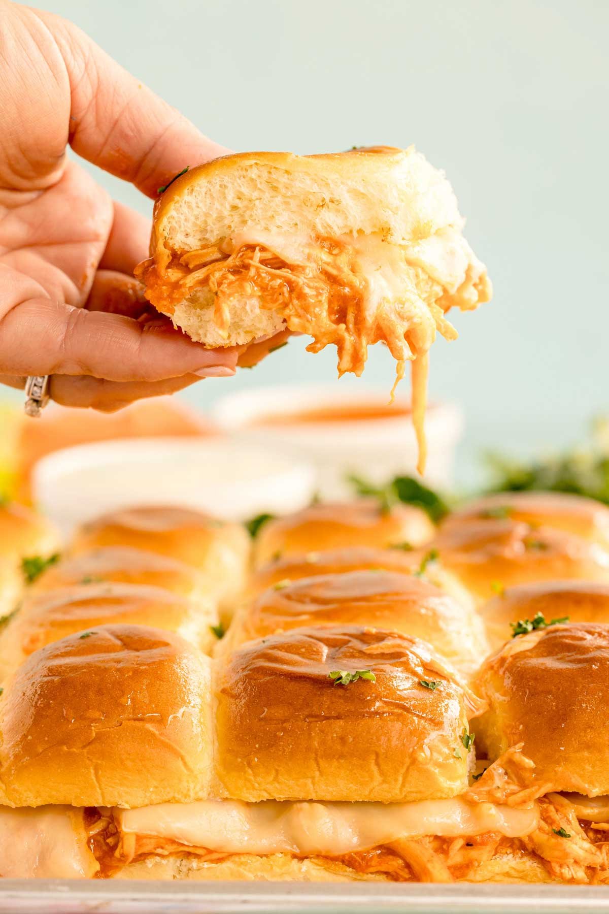 hand holding a buffalo chicken slider above a tray of sliders