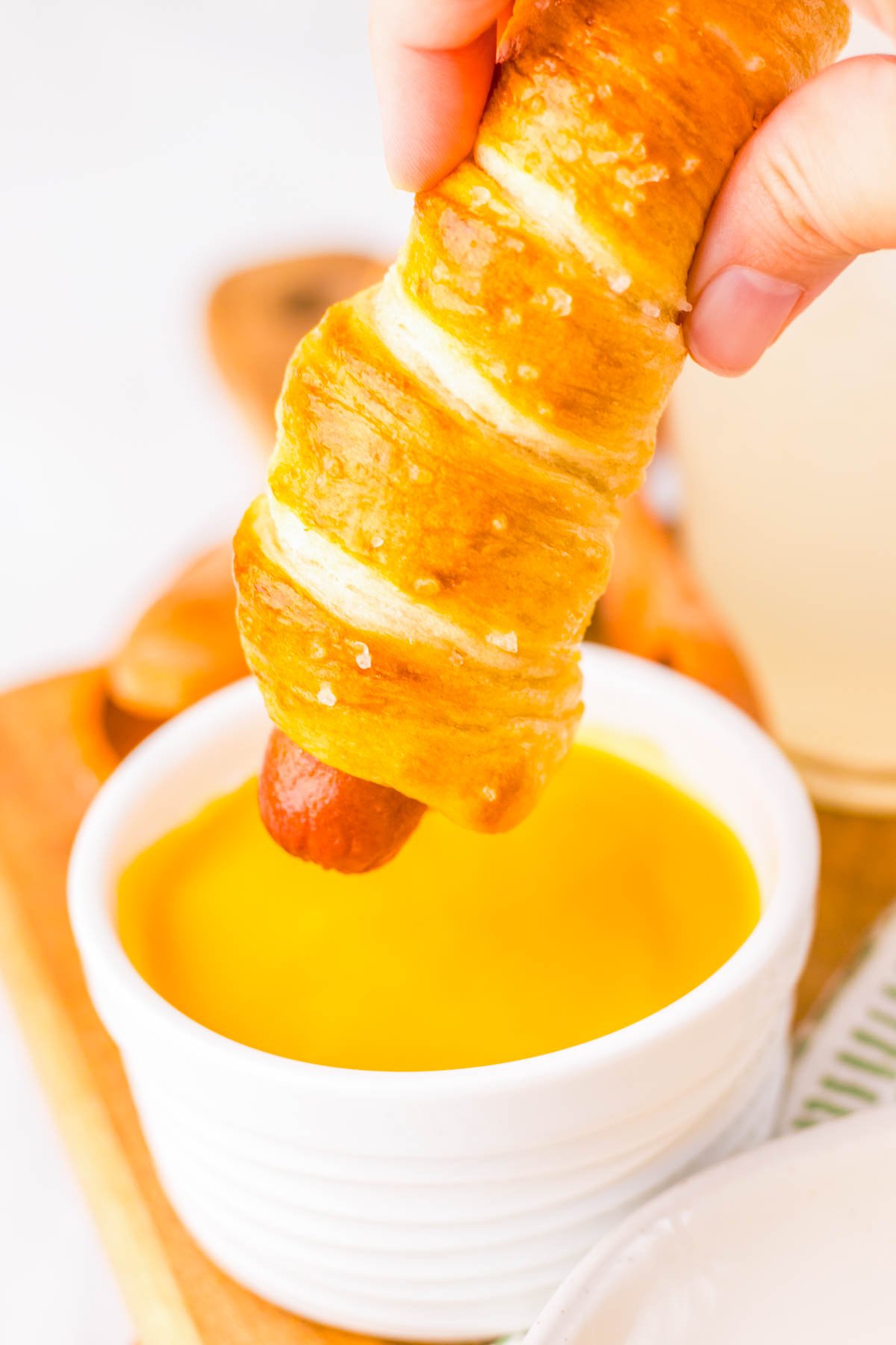 hand holding a pretzel dog above a cheese sauce