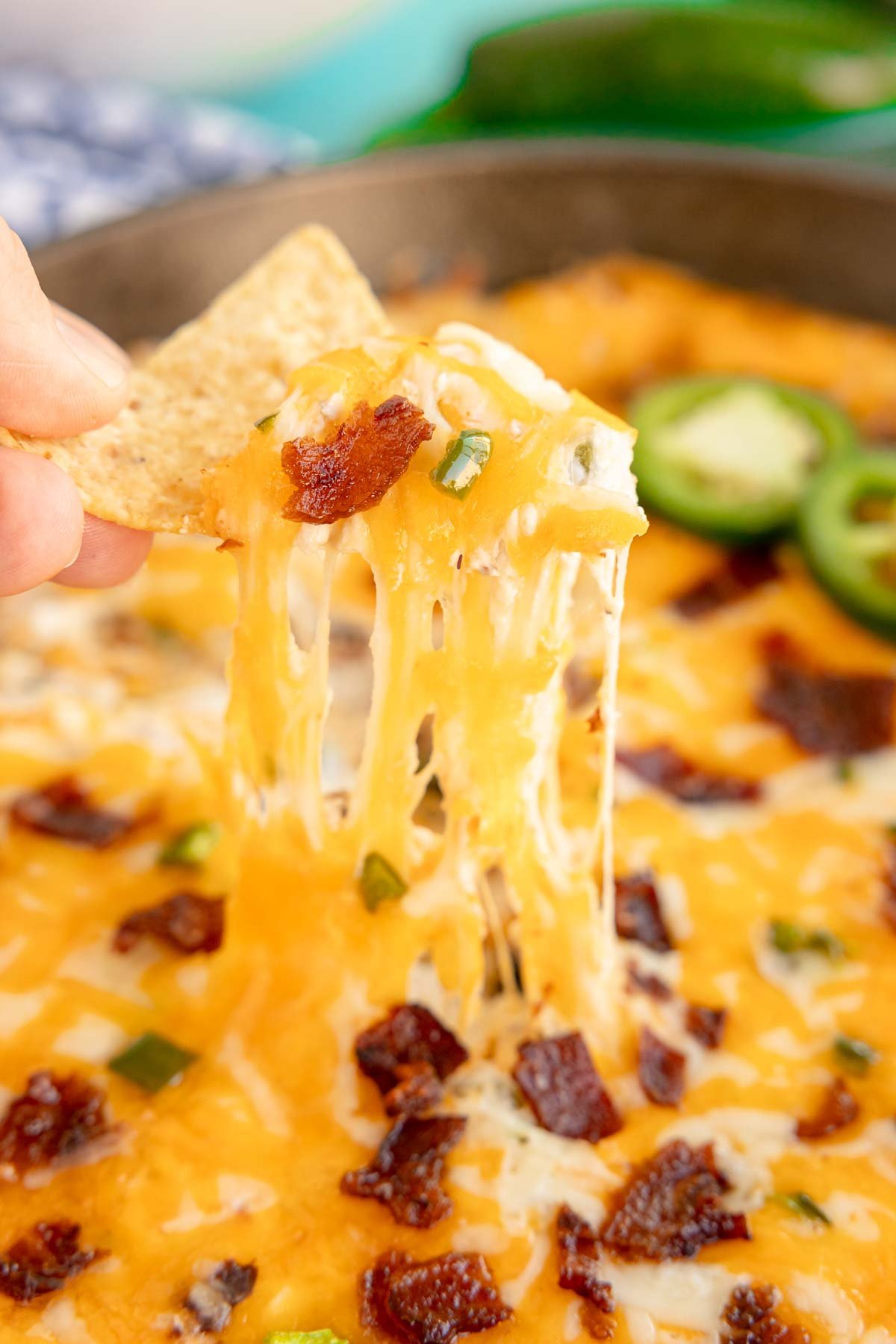 hand holding a chip dipped in a jalapeno popper dip in a skillet