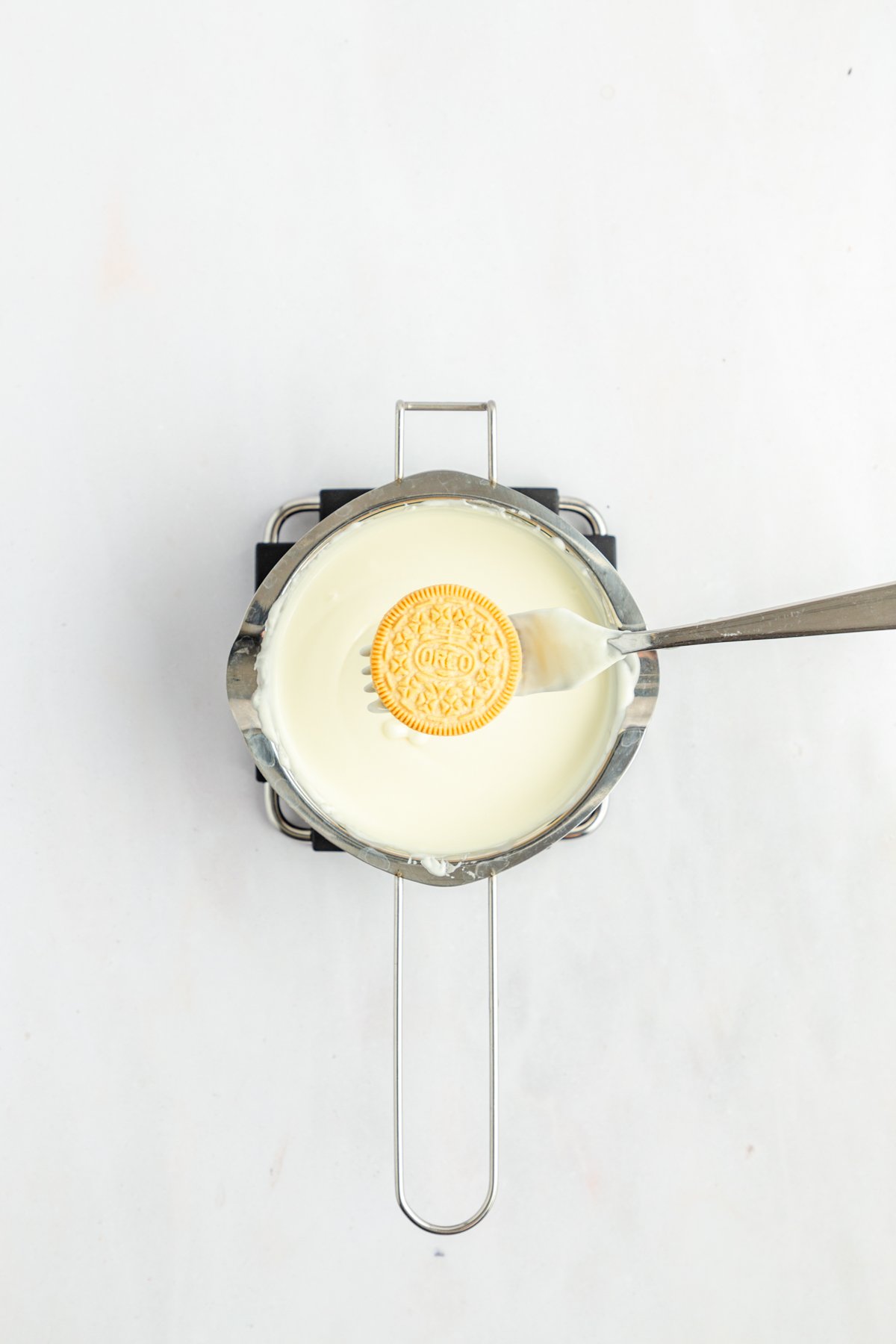 golden oreo on a fork above a pot of melted white chocolate