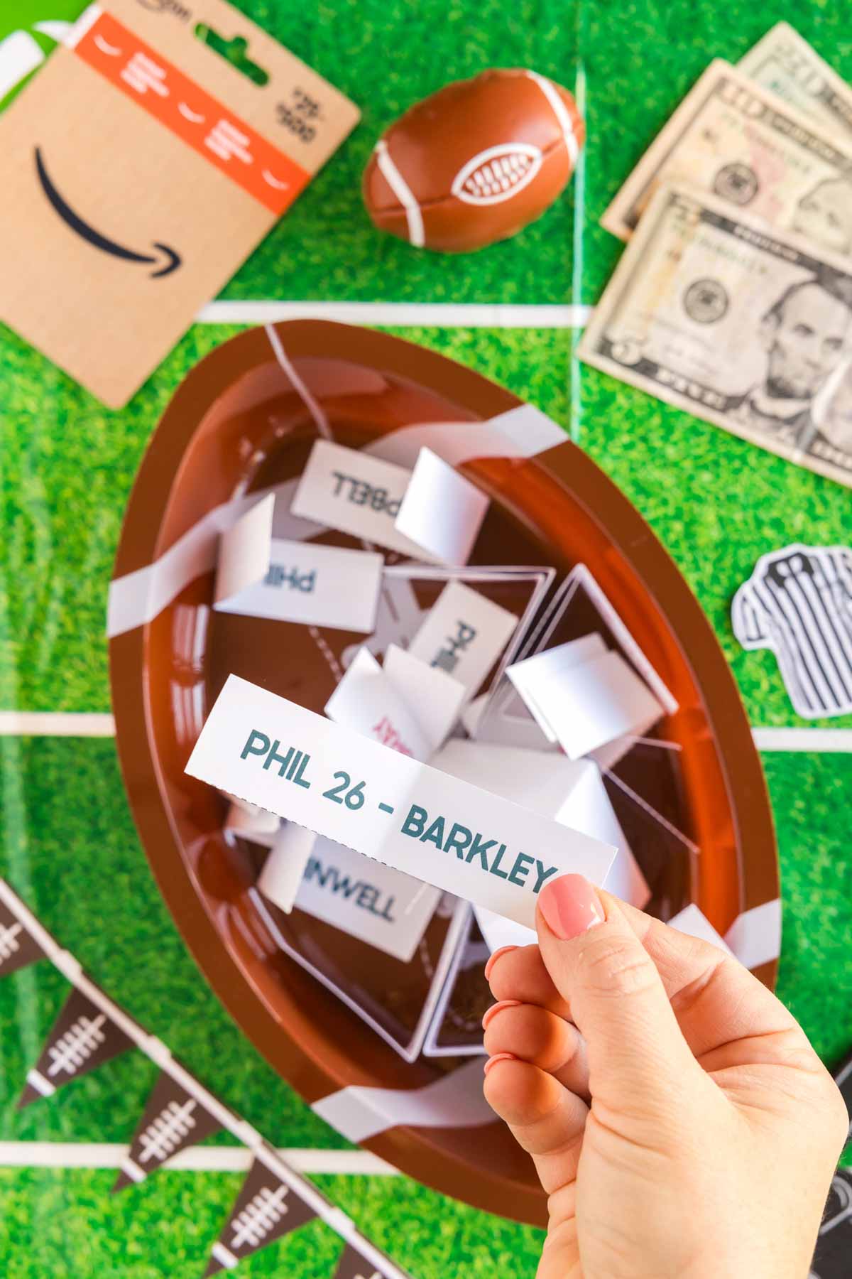 hand holding a piece of paper with jalen hurts name on it over a football filled with folded papers 